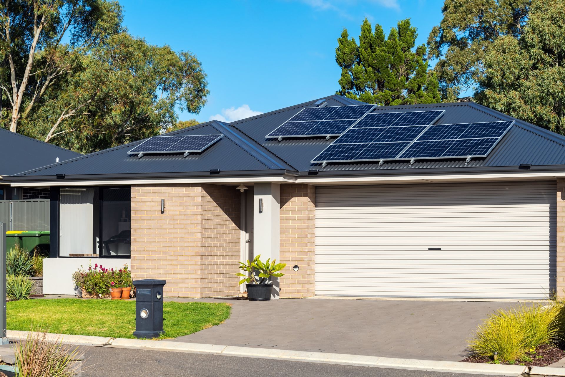 House with solar panels on roof, garage door, green yard, and blue sky.