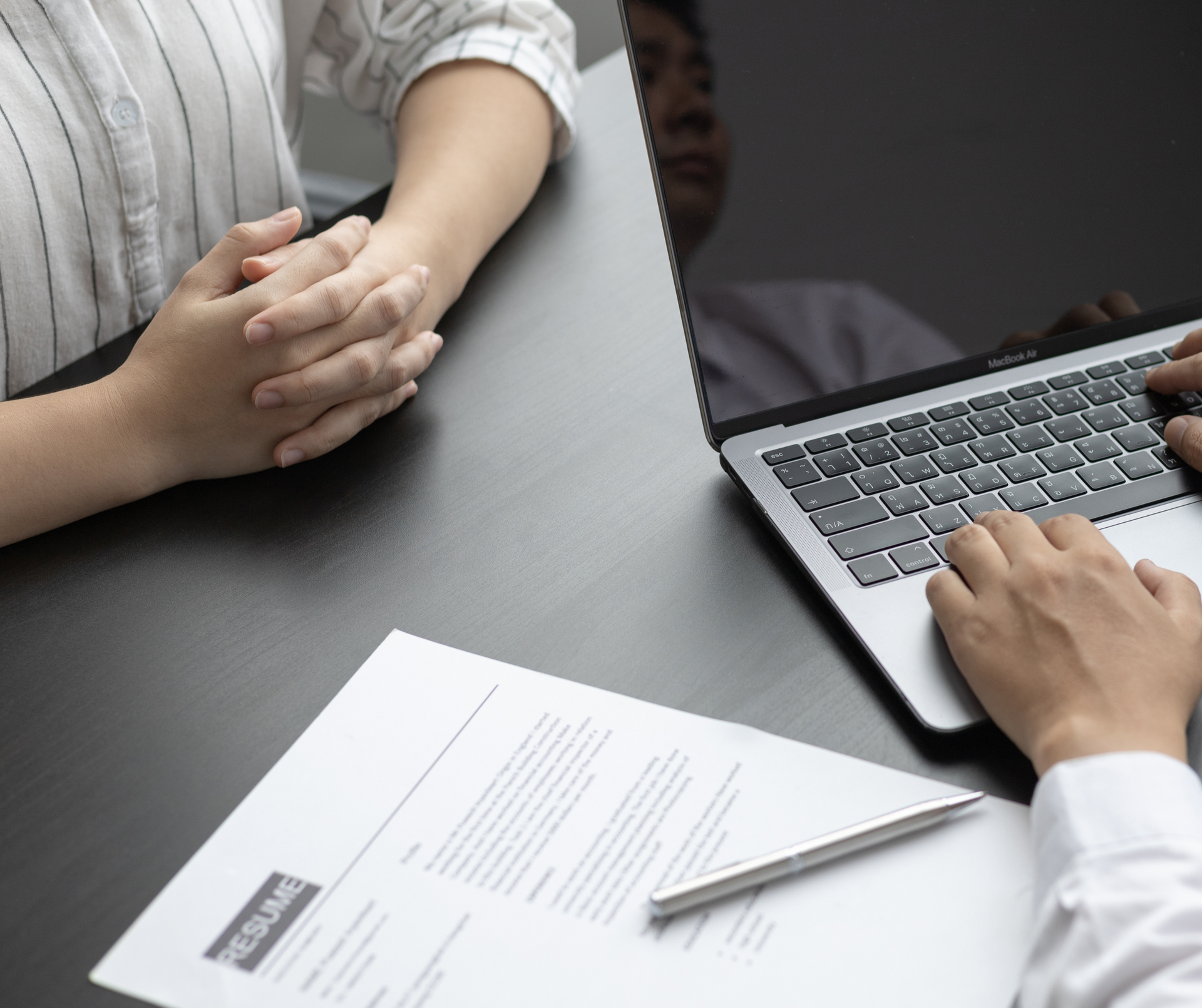 Two people in a job interview with a resume, pen, and laptop on a desk, showing a hiring decision