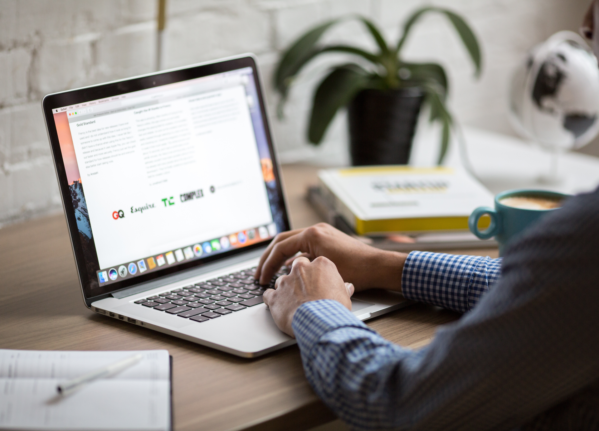 Person typing on a laptop while writing or editing content at a desk with coffee and notebooks.