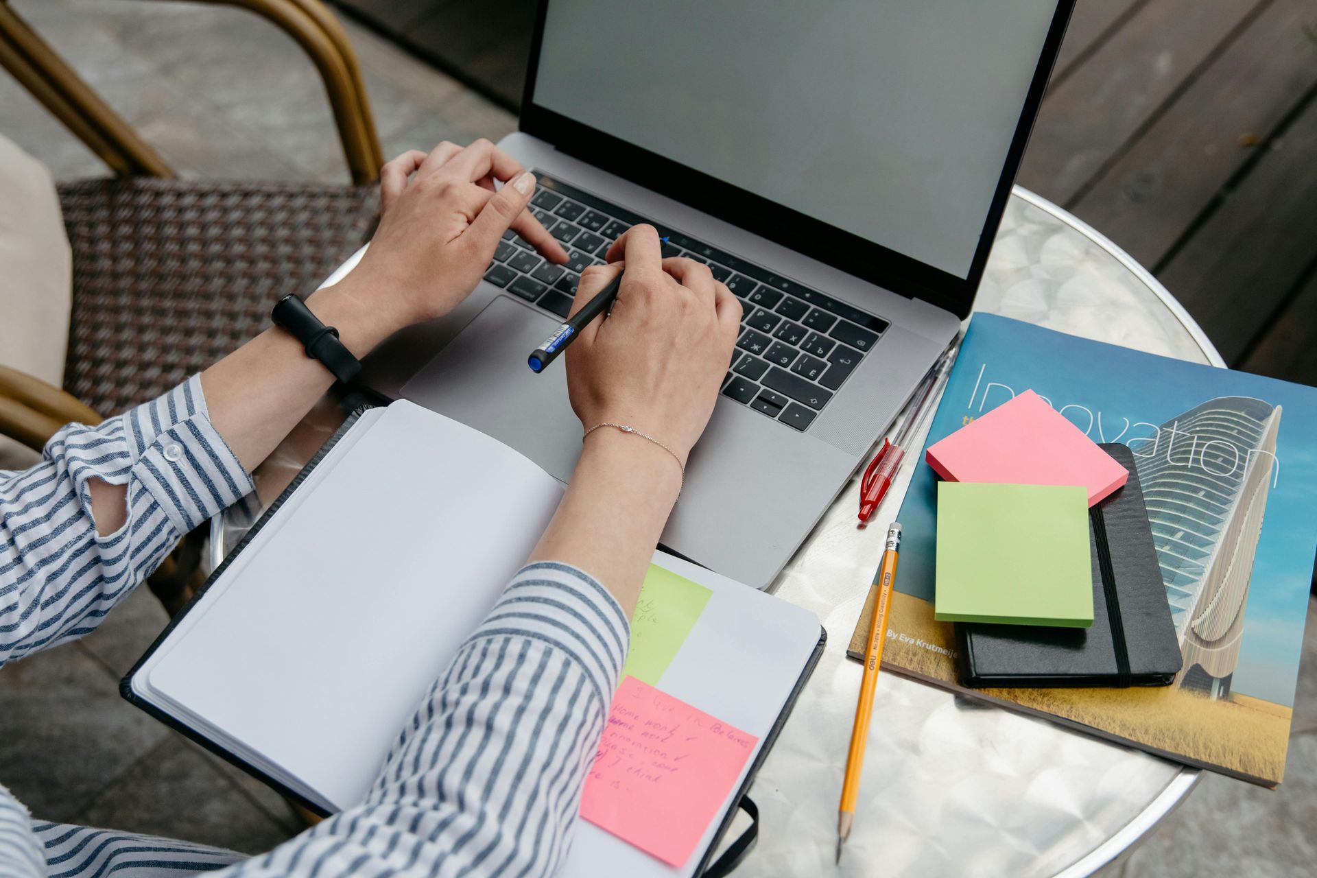 Person working on a laptop with notebooks, sticky notes, and a magazine on a desk, representing goal
