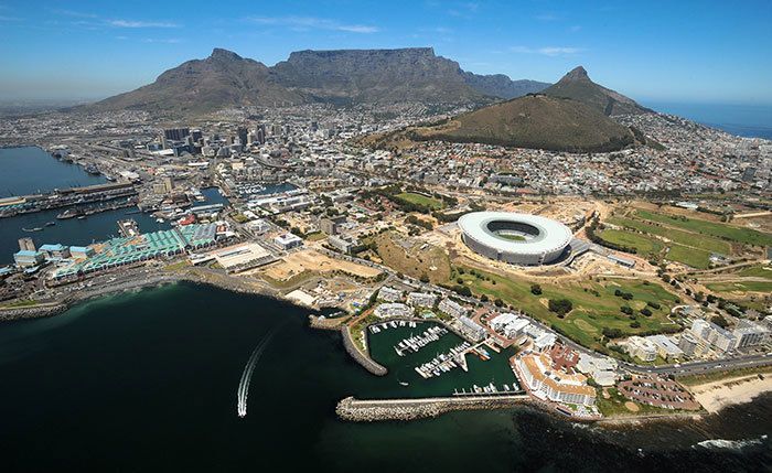 Aerial view of Cape Town, South Africa, with Table Mountain in the background, a stadium, and harbor.