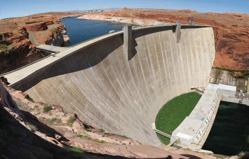 Glen Canyon Dam curves across a canyon, reservoir above, structure of concrete and walkway on top.