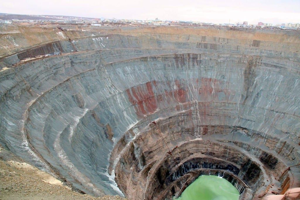 Large, open-pit diamond mine with layered rock walls. A pool of green water at the bottom.