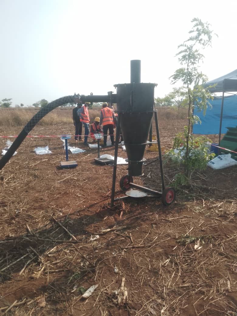 A black cyclone dust collector with people nearby, standing on a brown field.