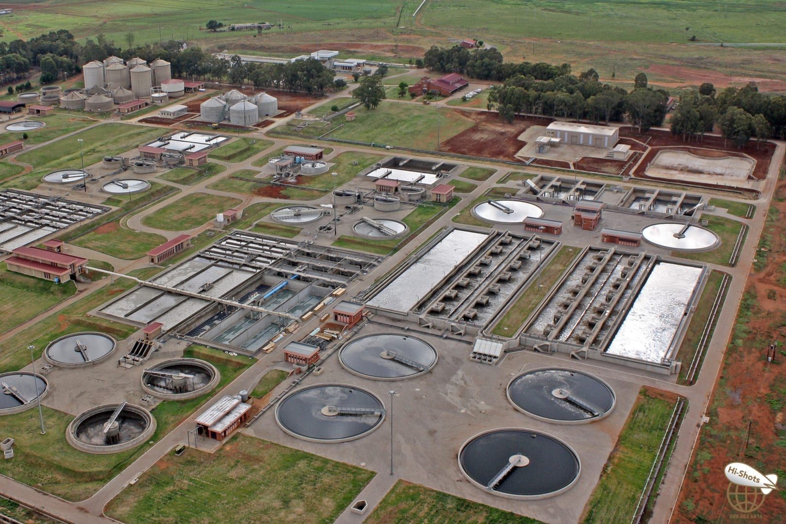 Aerial view of a wastewater treatment plant with various tanks, buildings, and green space in a rural setting.