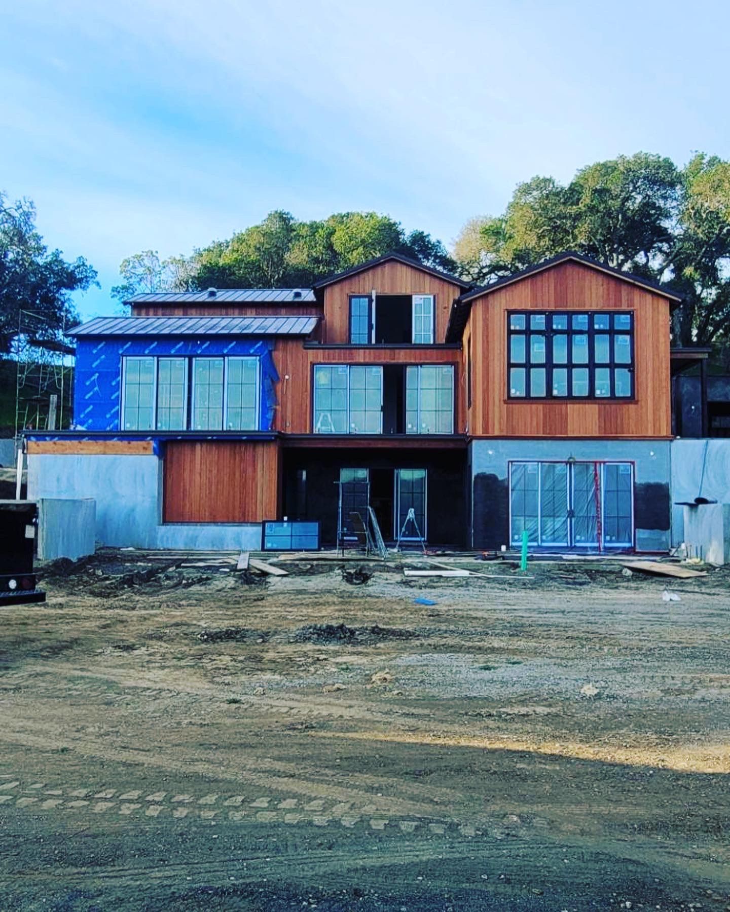 Modern house under construction with wood siding, large windows, and unfinished landscaping.