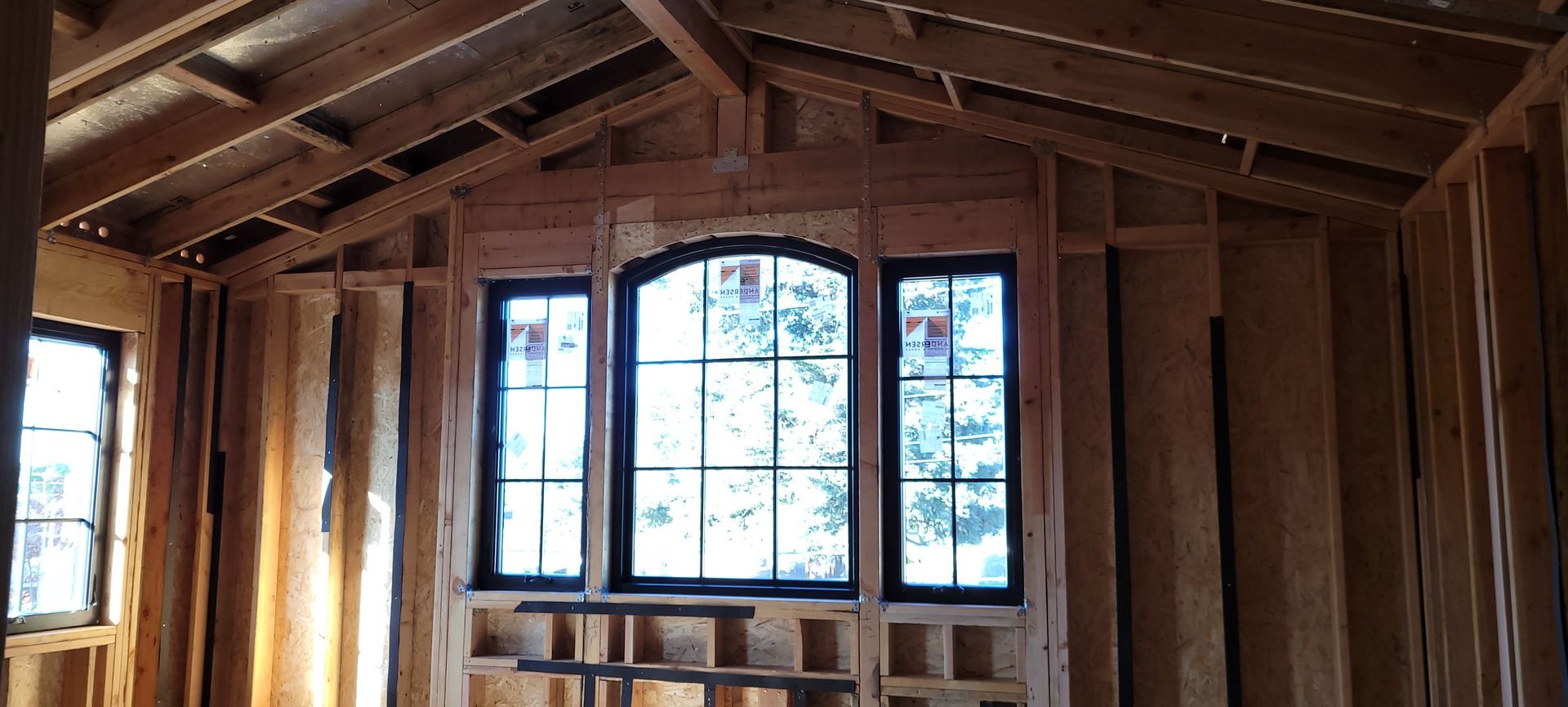 Interior framing of a room with windows; wooden beams and studs.