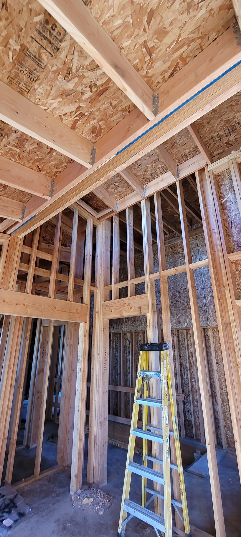 Interior view of wooden house framing in progress, yellow ladder is leaning against the wall.