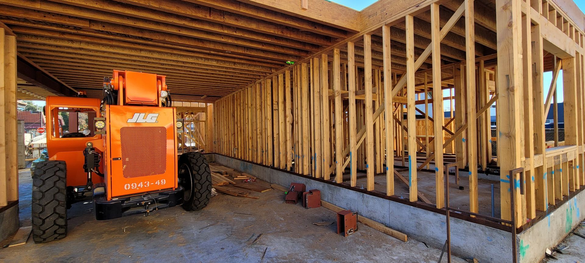 An orange construction forklift inside a wood-framed building under construction.