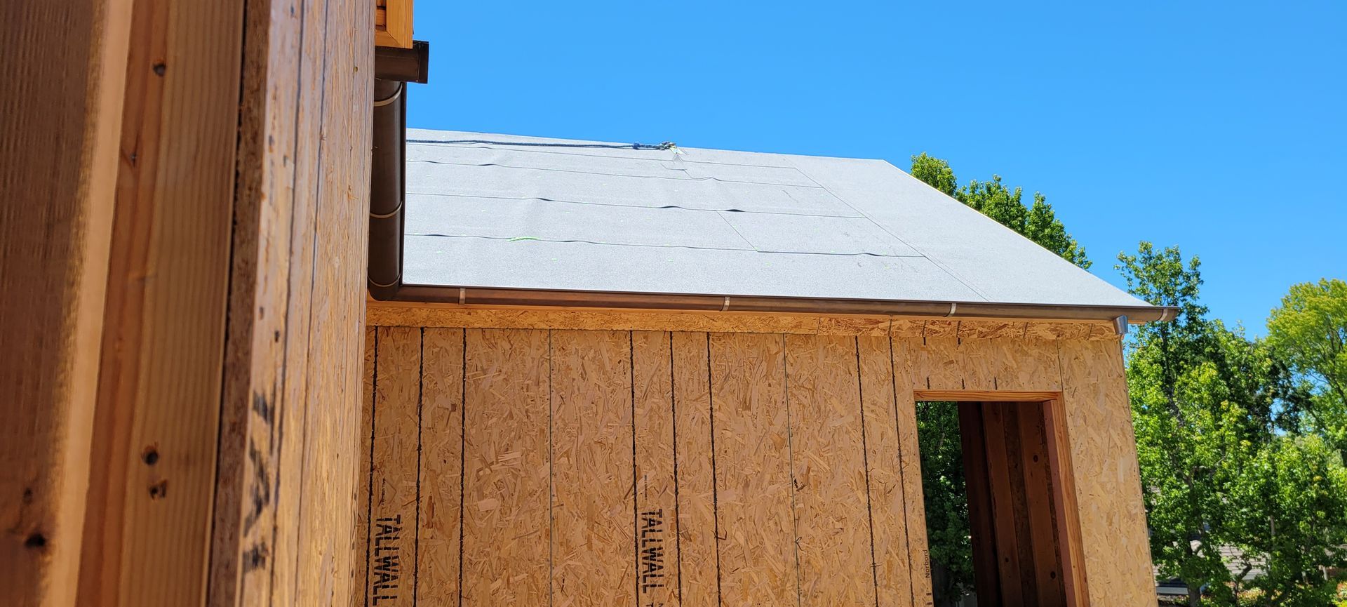 Exterior view of a building under construction, featuring wooden framing, and a clear blue sky.