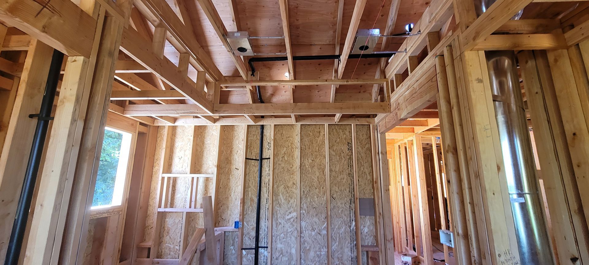 Interior view of a building under construction, showing wooden framing and exposed ceiling beams.