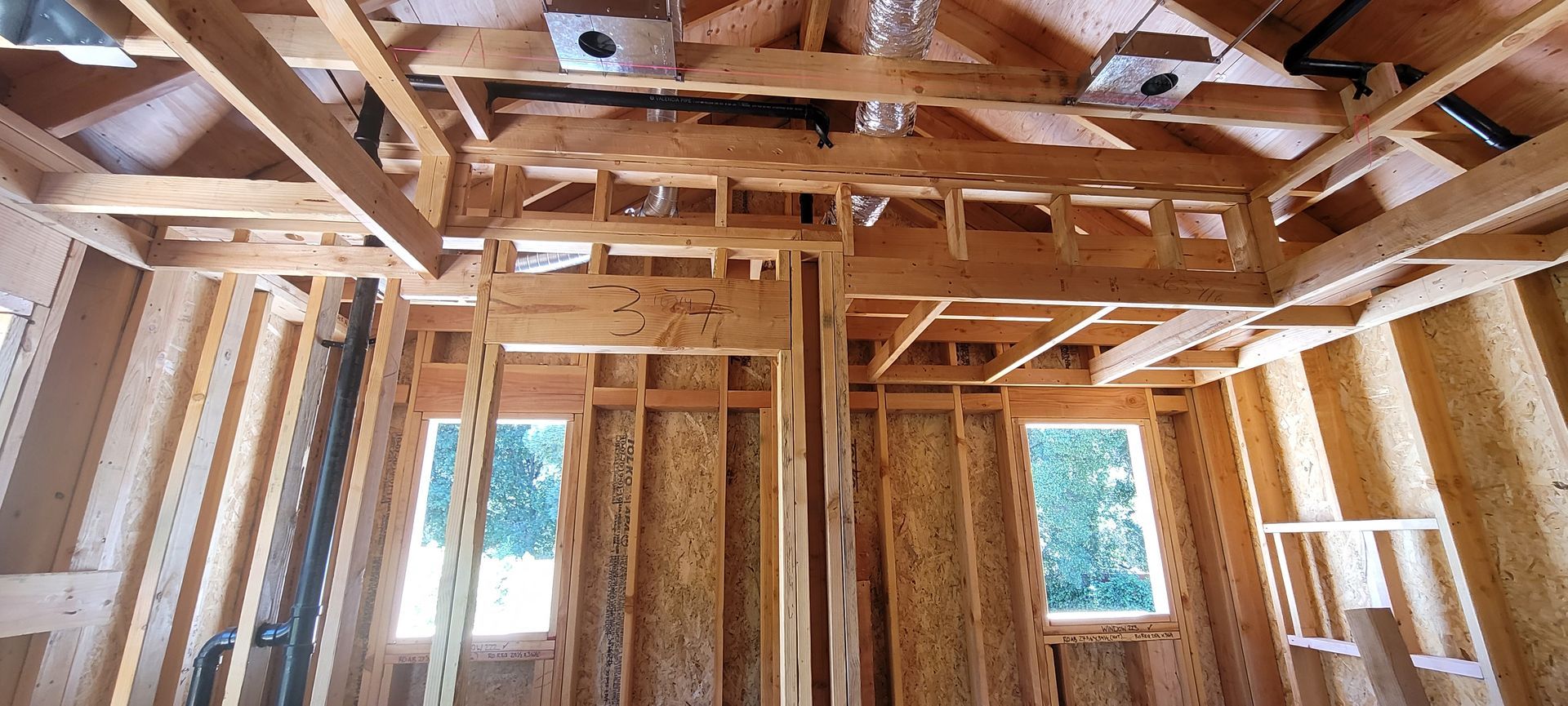 Interior view of a building under construction, framed with wooden beams, showing windows and ventilation.