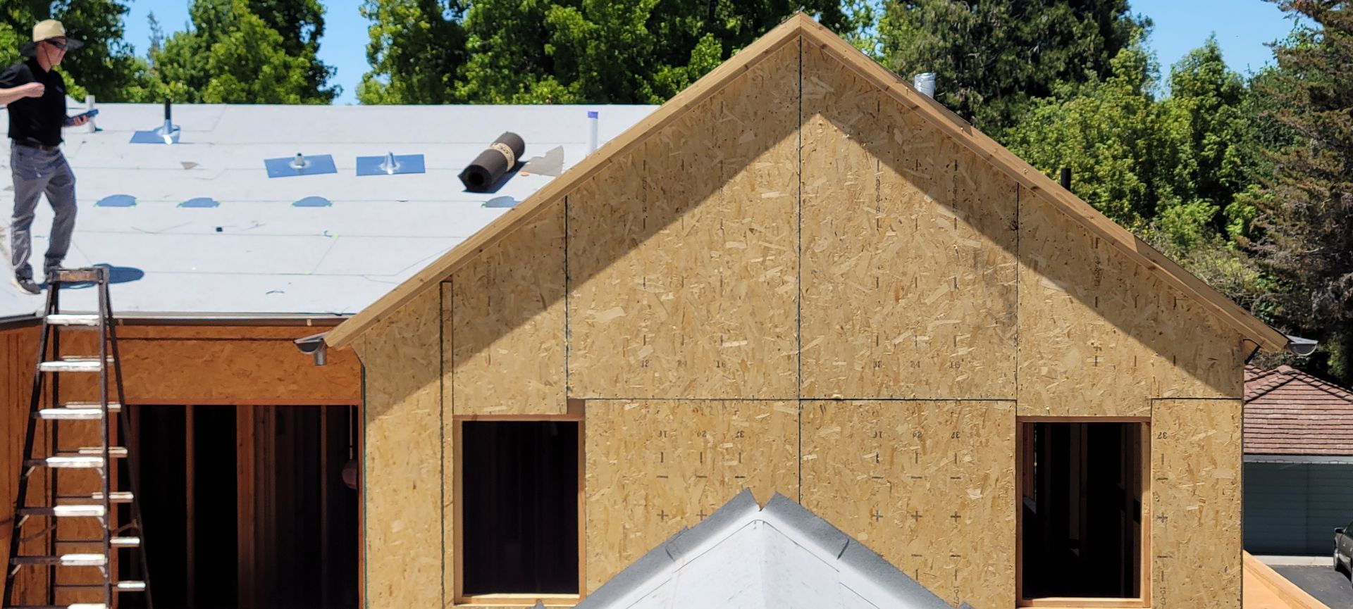 A partially built house with a worker on the roof. The house is brown and the roof is white.