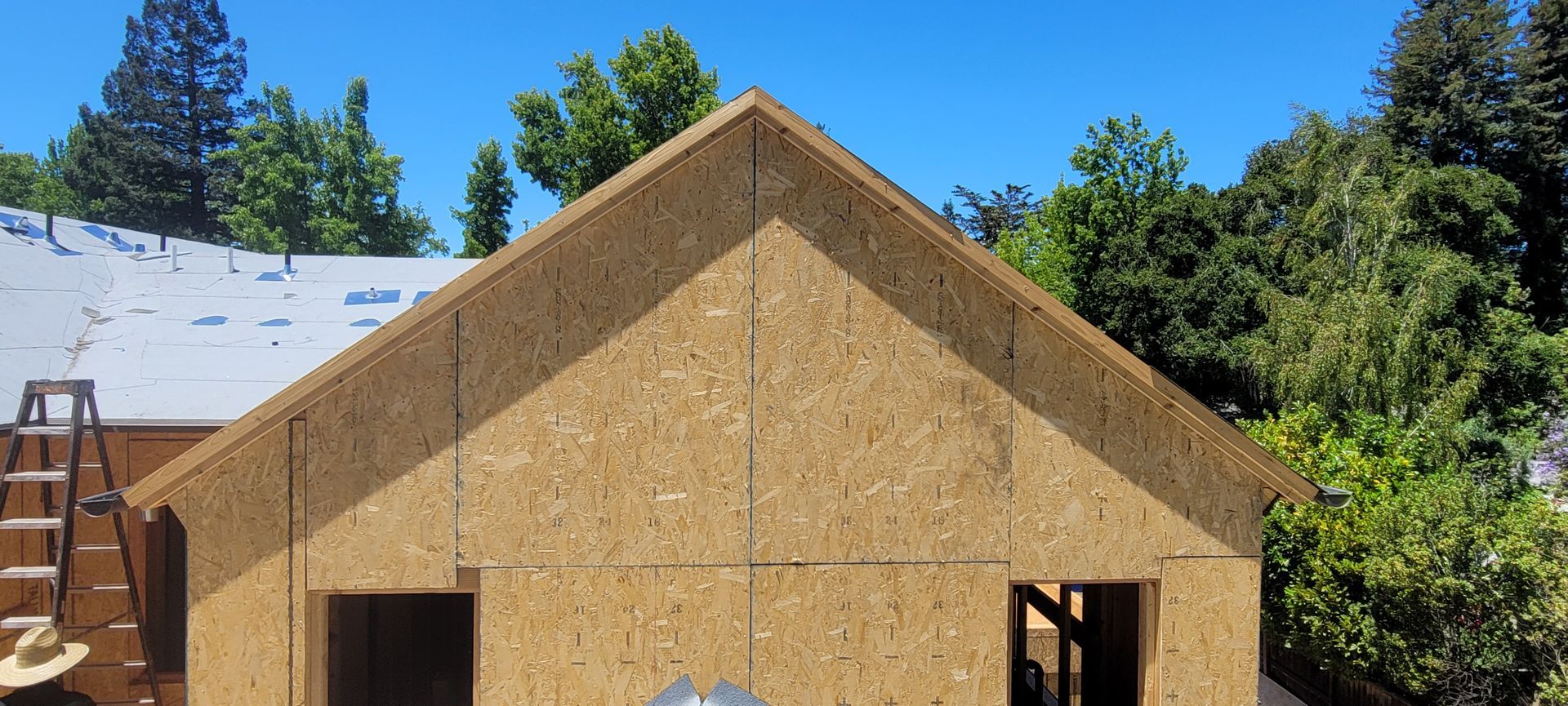 Exterior view of a building in progress, with wooden walls and a roof frame, under a blue sky.