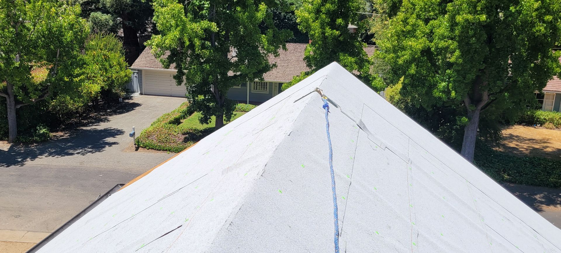 View of a white roof with a neighborhood in the background, trees surround the houses on a sunny day.