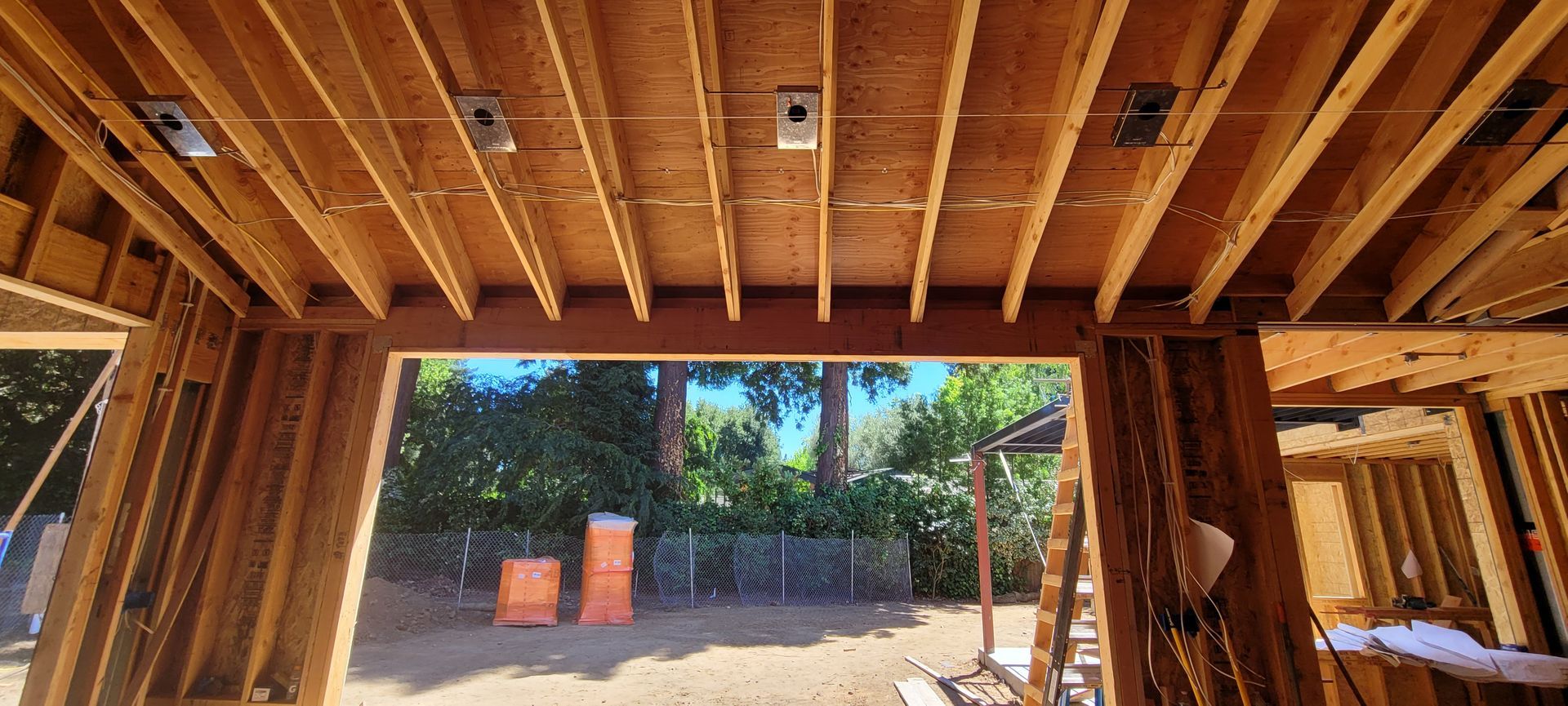 Interior view of a building under construction, showing wooden framing, an open doorway, and outdoor scenery.
