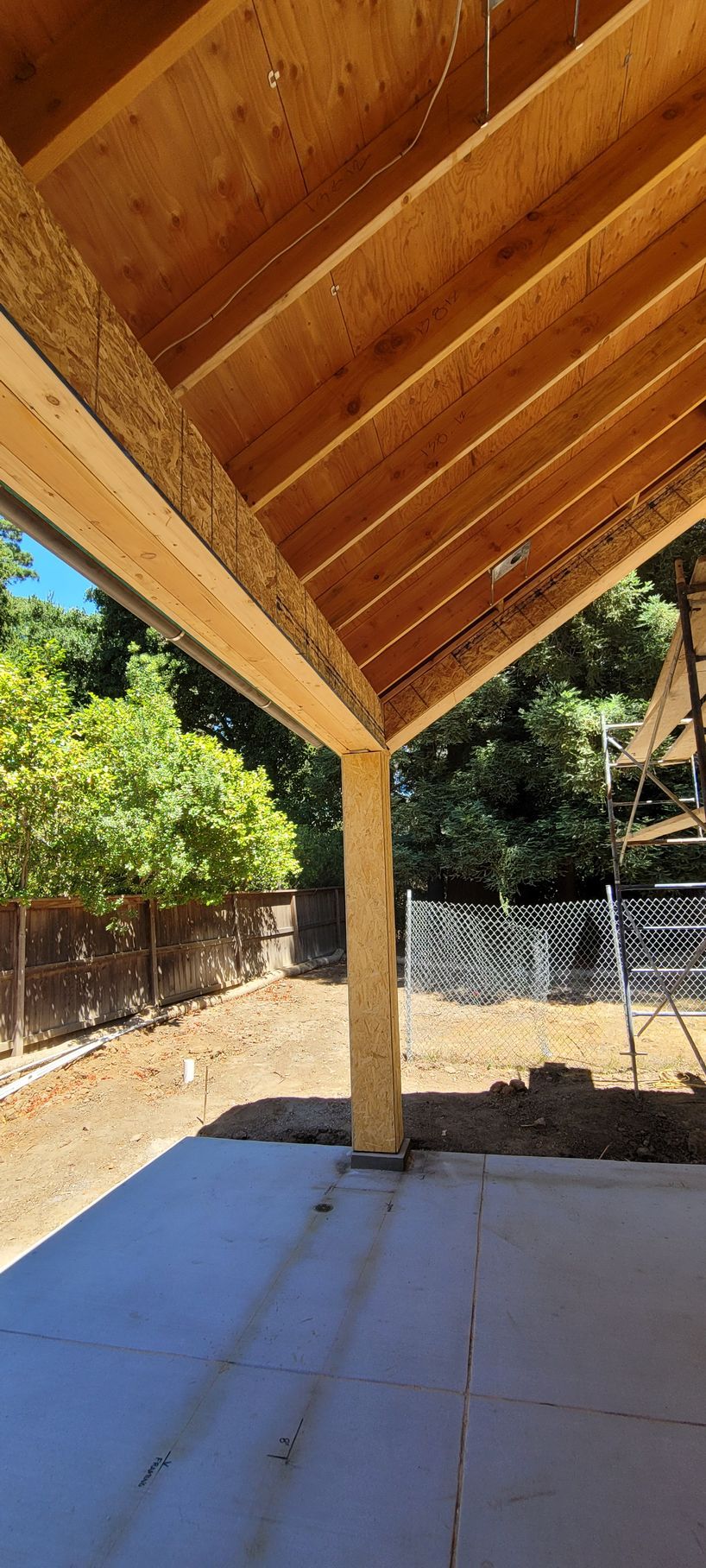 Construction of a covered patio with wooden beams and a concrete floor. 