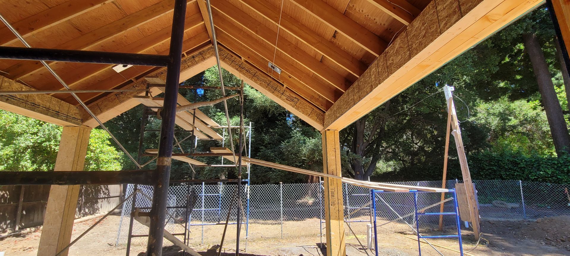 Construction of a wooden structure; exposed beams, scaffolding, and surrounding trees.