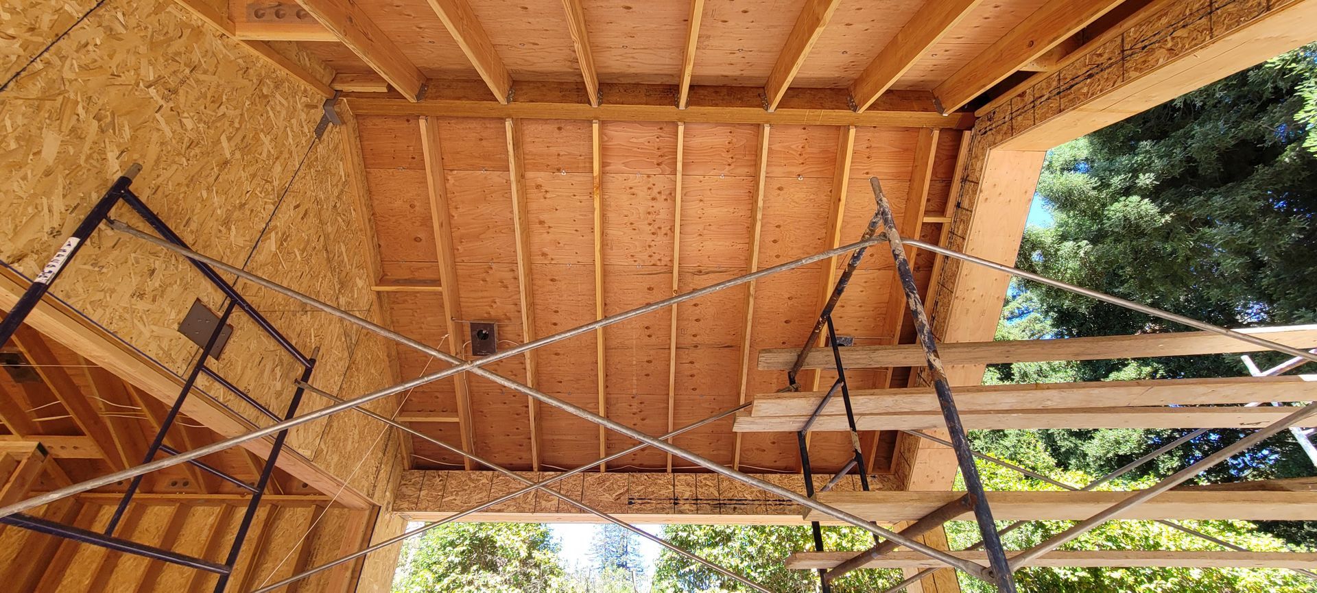 Wooden framework of a building's ceiling and walls. Construction site, with scaffolding and outdoor view.