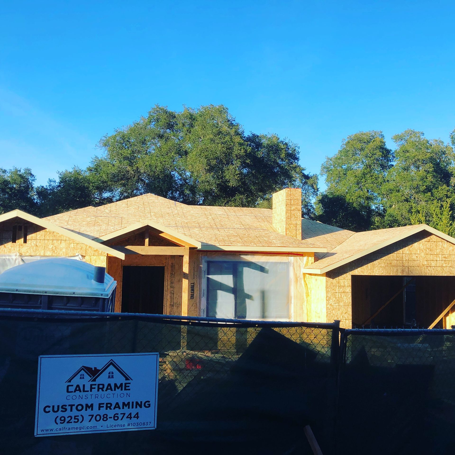 House under construction behind a chain-link fence on a sunny day.