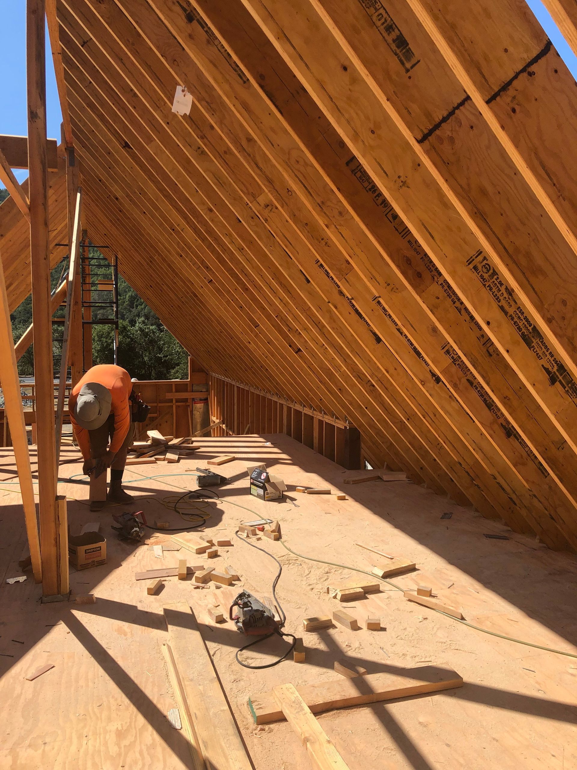 Construction worker on roof frame with tools and wood. Sunny outdoor setting.