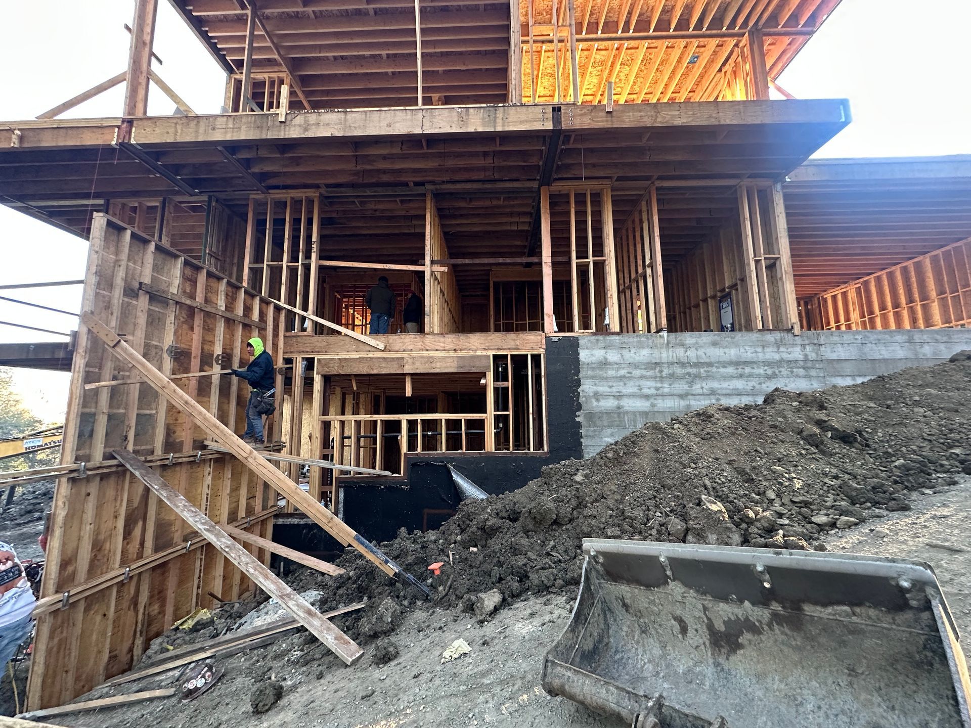 Wooden frame of a house under construction on a concrete foundation, lumber scattered on the ground.