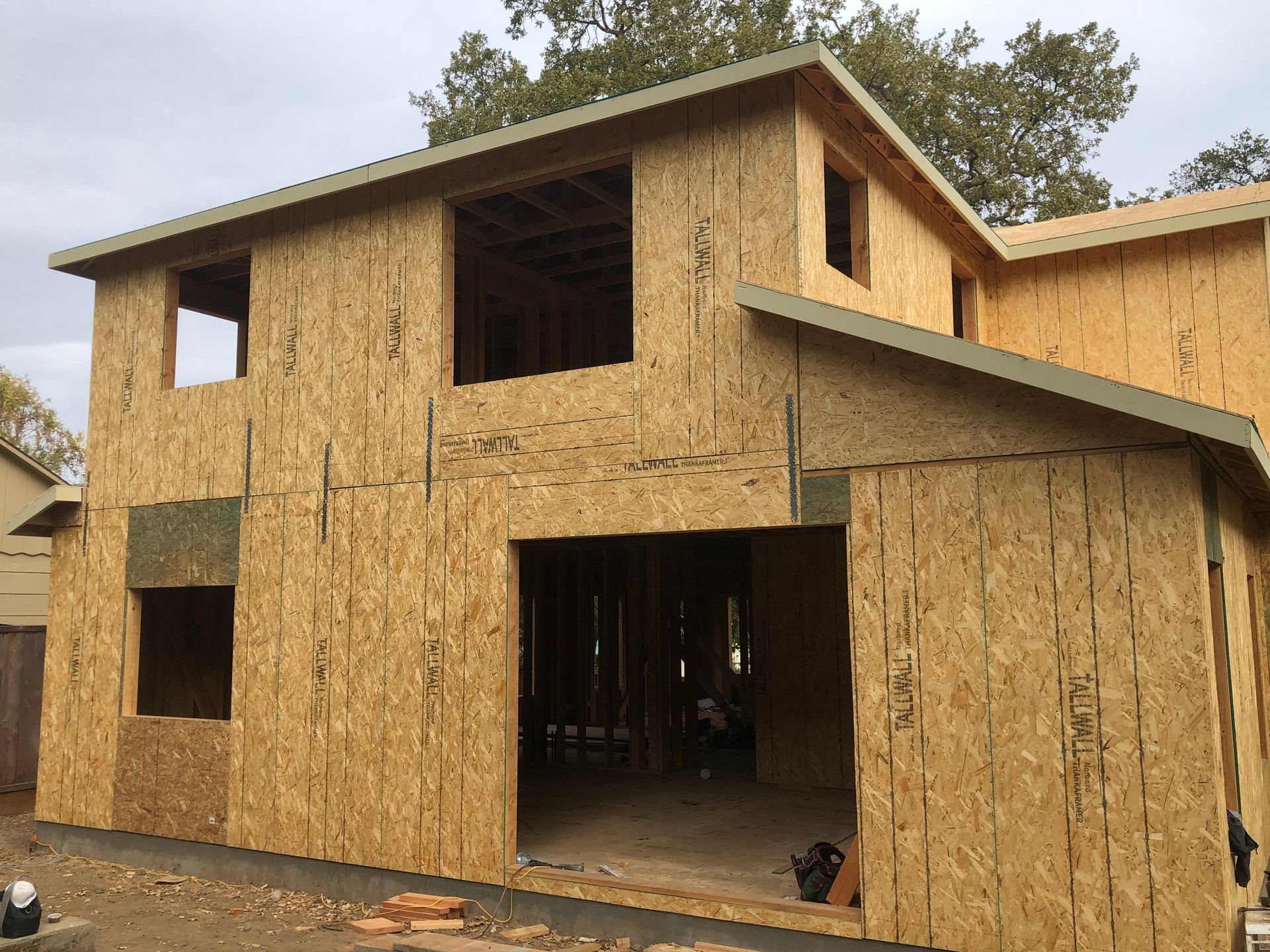 Construction of a two-story house, exterior view. OSB sheathing covers the frame, with window and door openings.