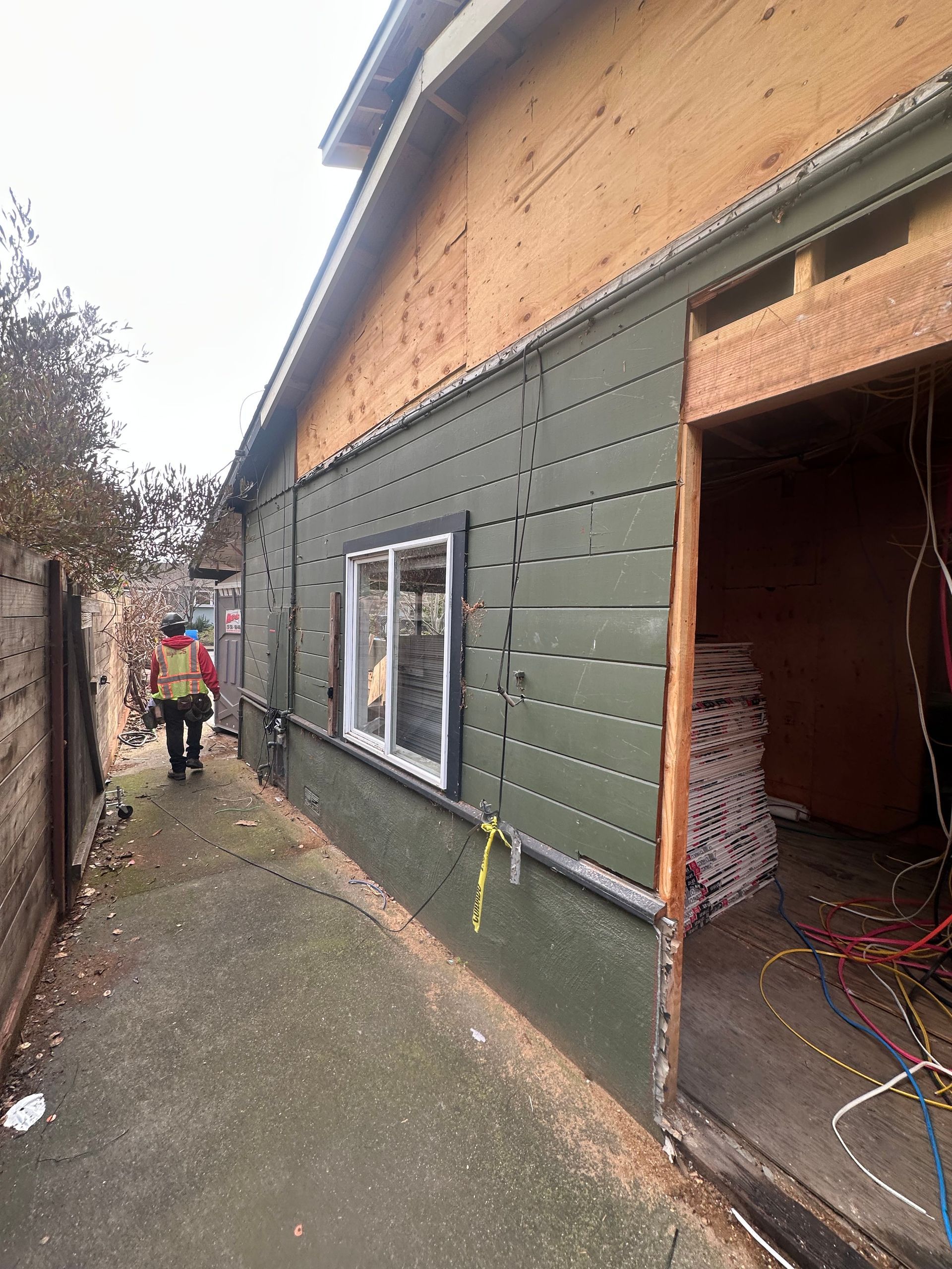 Exterior of a building under renovation with green siding, a window, and open doorway; worker walks nearby.
