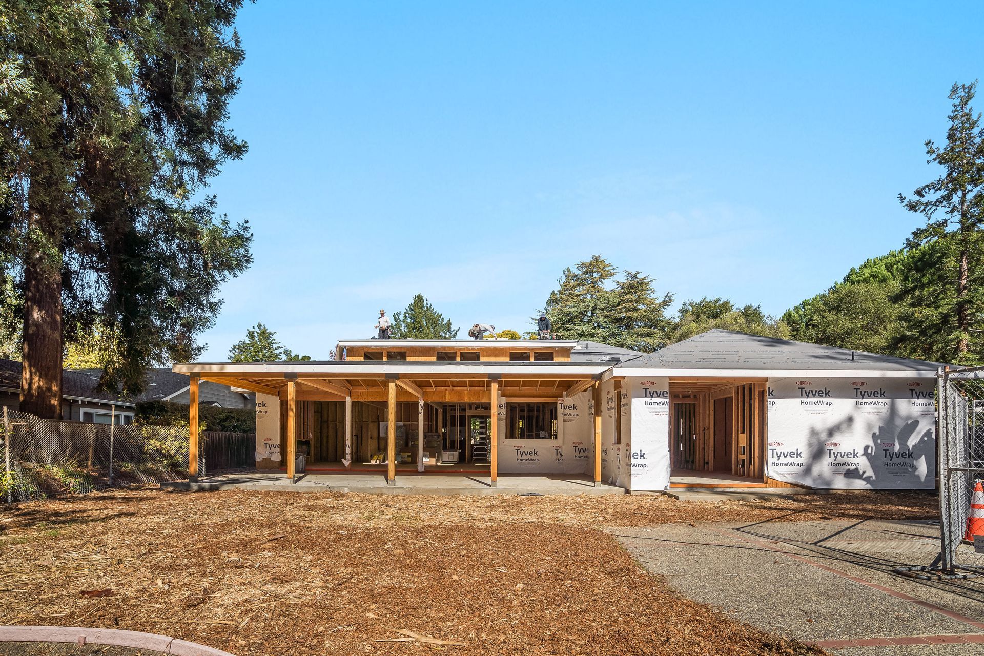 House under construction, exterior view with wooden framework, covered porch, and blue sky.
