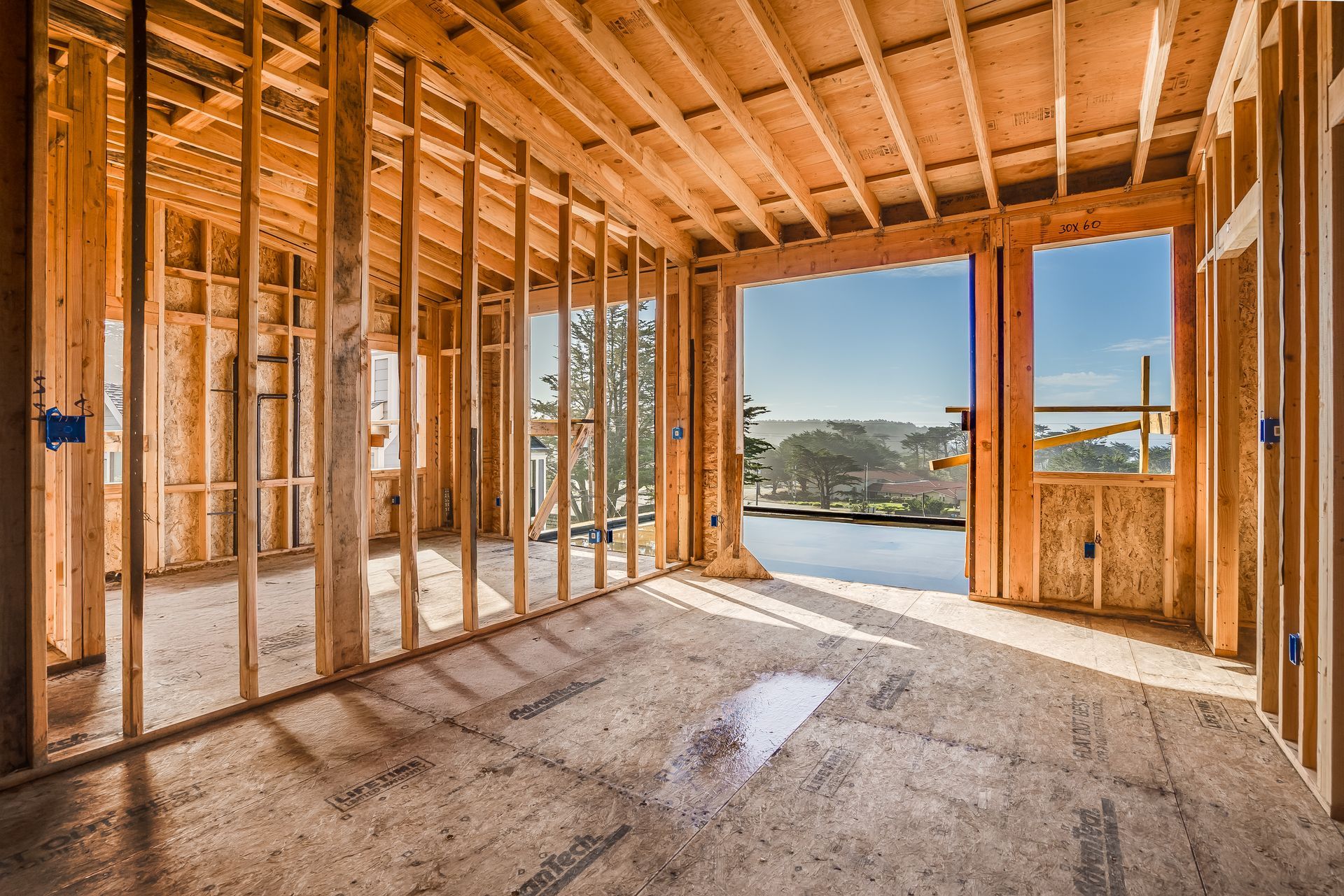 Interior of a building under construction, wooden frame, doorway opens to a sunny view of water and trees.