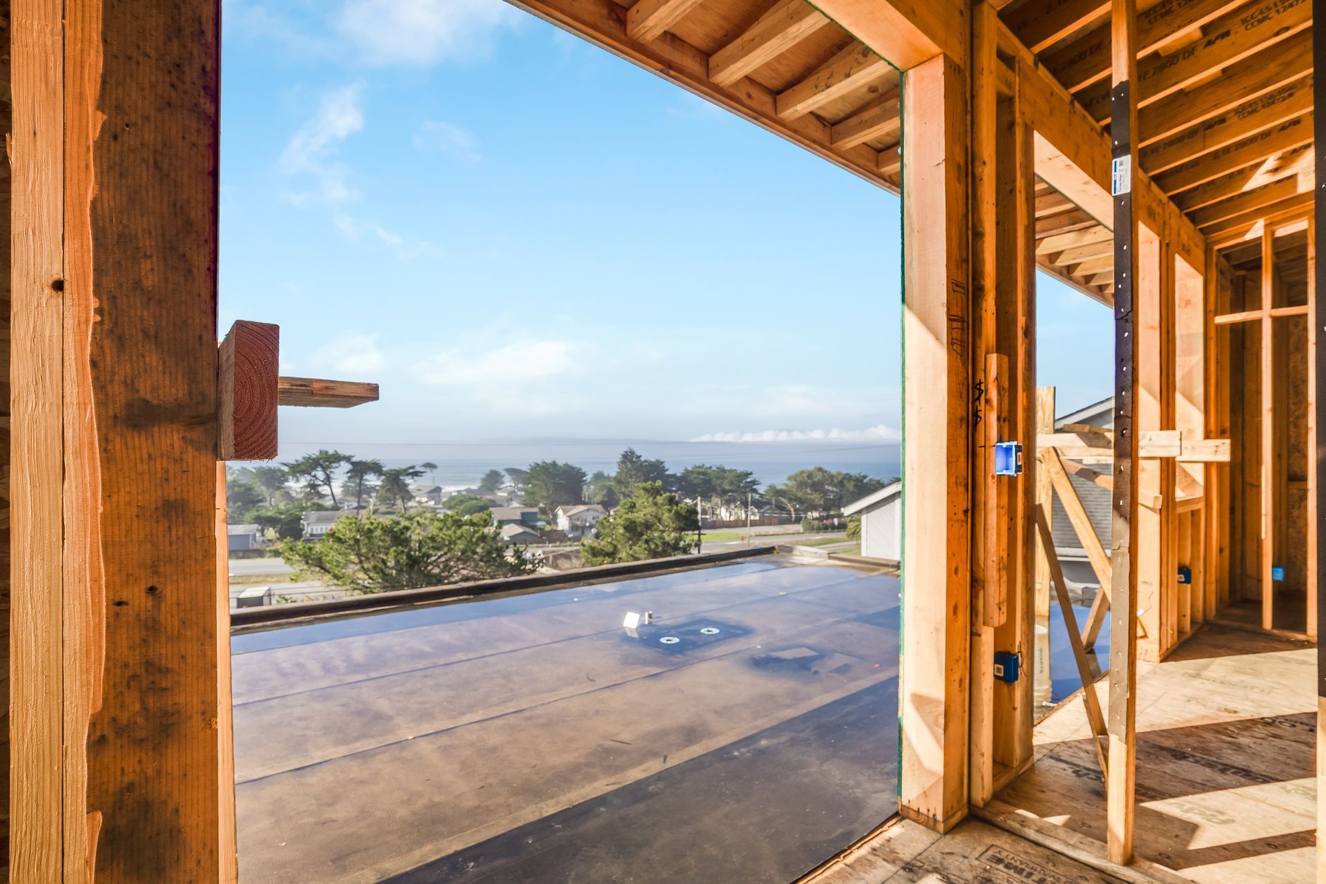 Wooden frame of a house under construction, with a view of the ocean and blue sky.