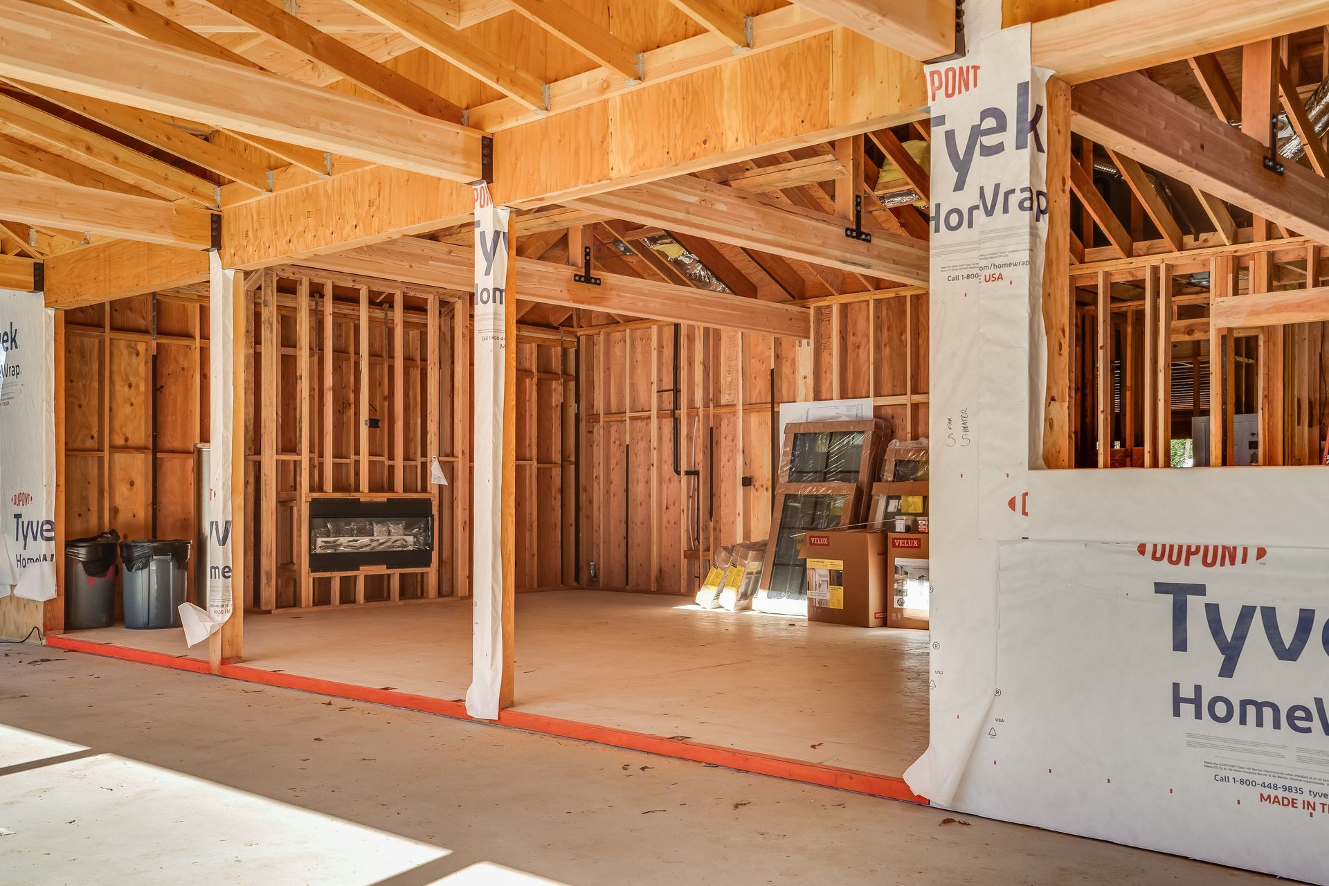 Interior of a home under construction. Wooden framing is visible, with Tyvek siding and concrete flooring.