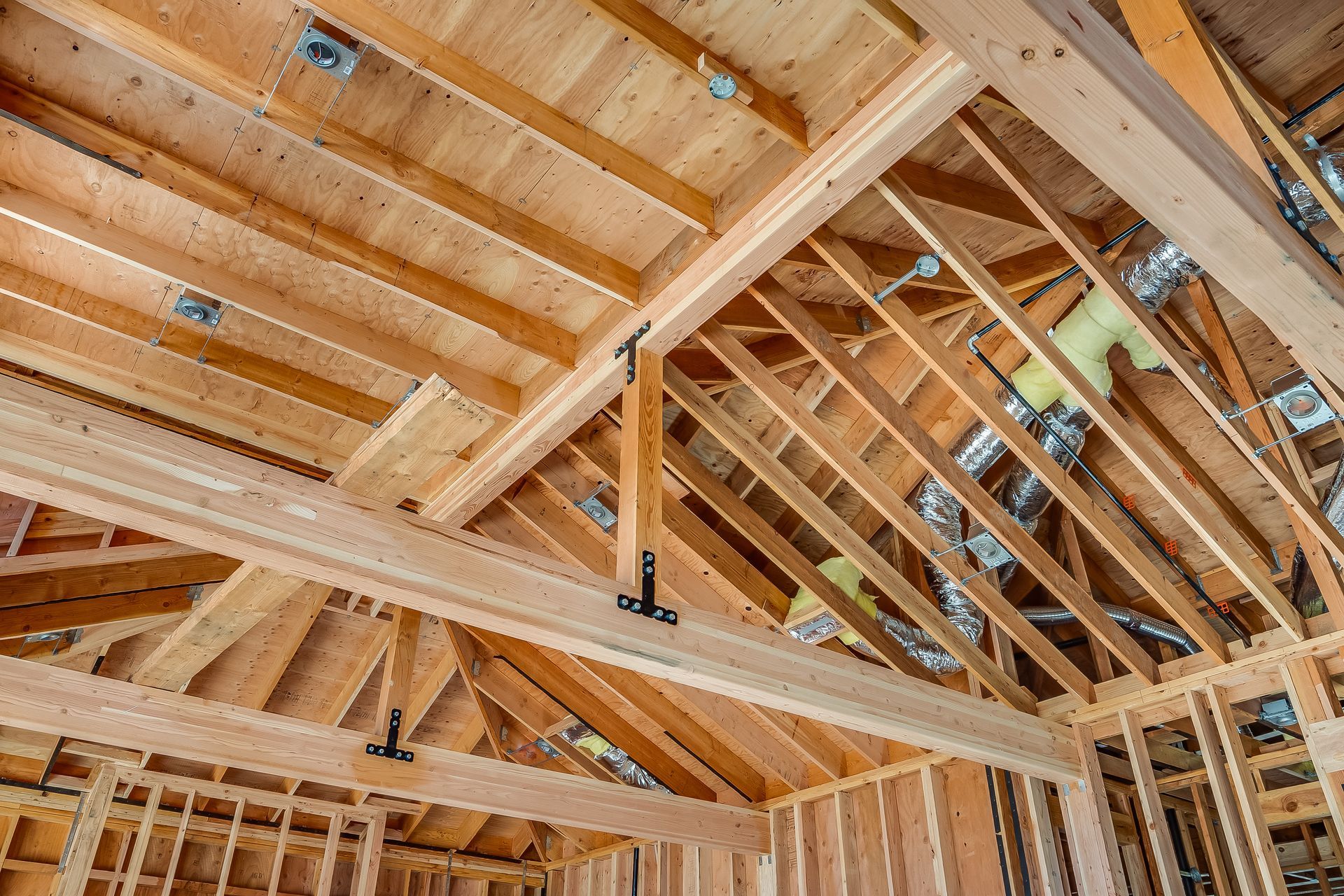 Wooden roof framing in progress, showing rafters, beams, and ceiling joists.