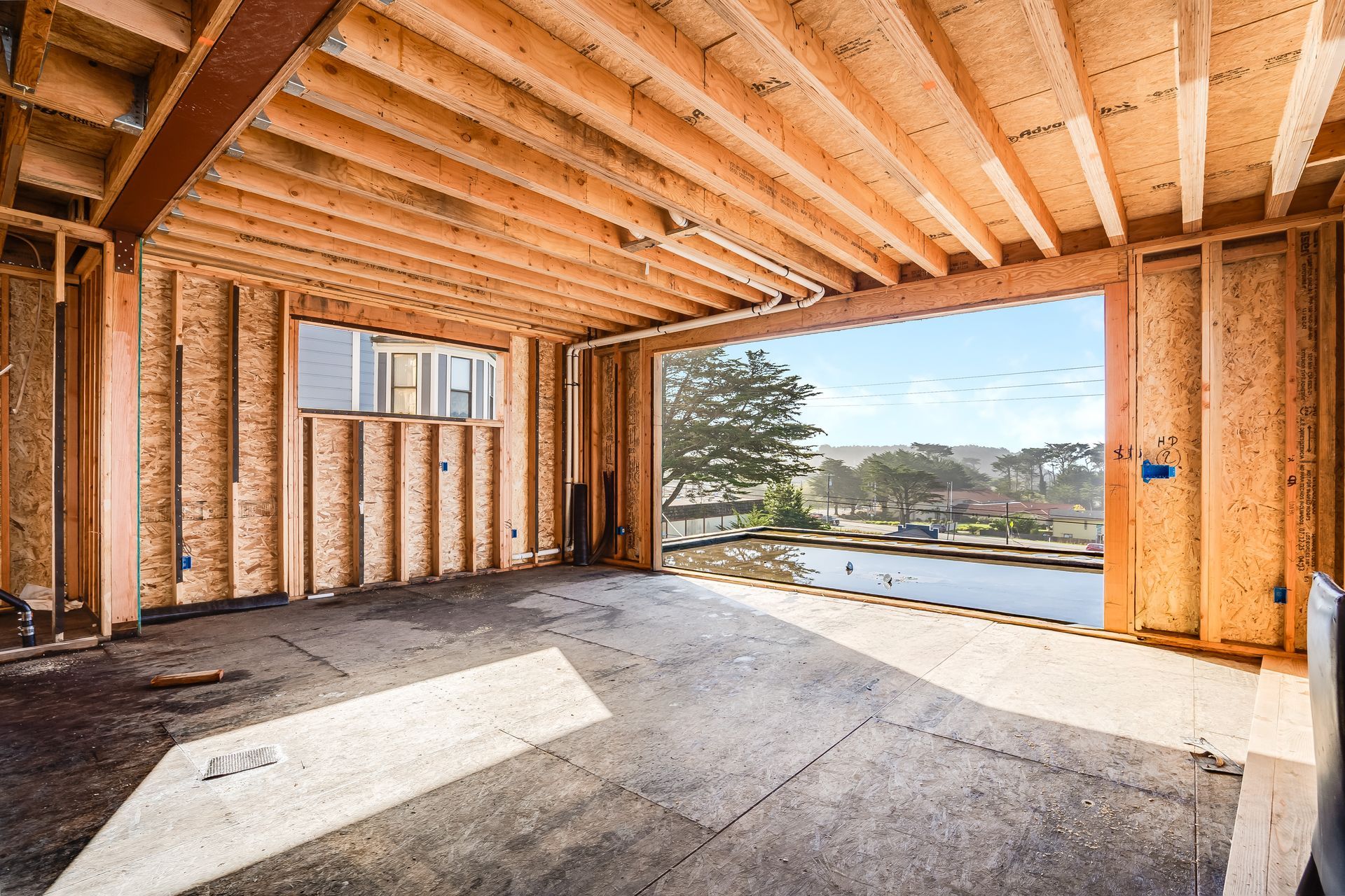 Interior of a building under construction, wooden framework with a large opening offering a scenic view.