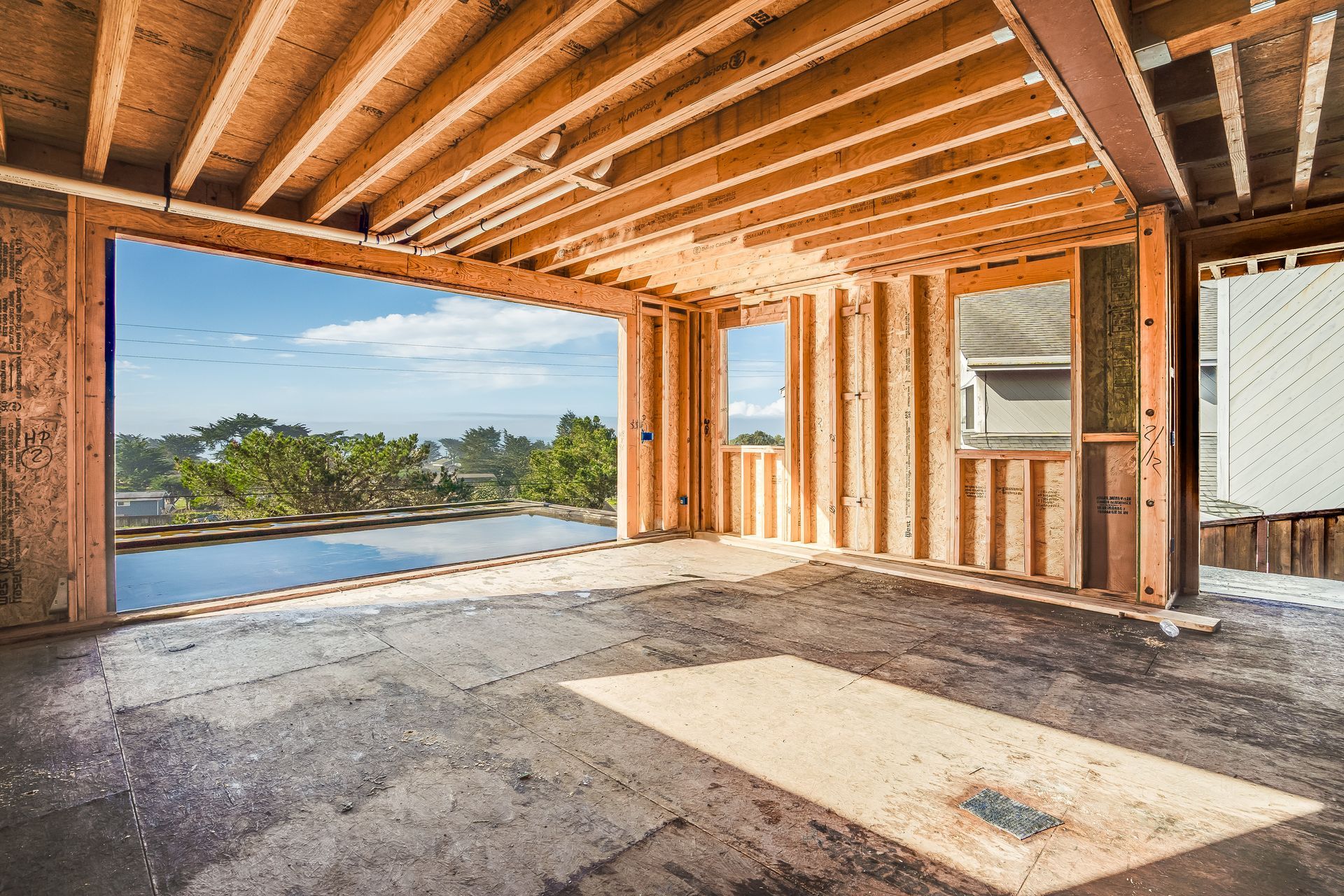Unfinished wooden building frame with ocean view through large opening. 