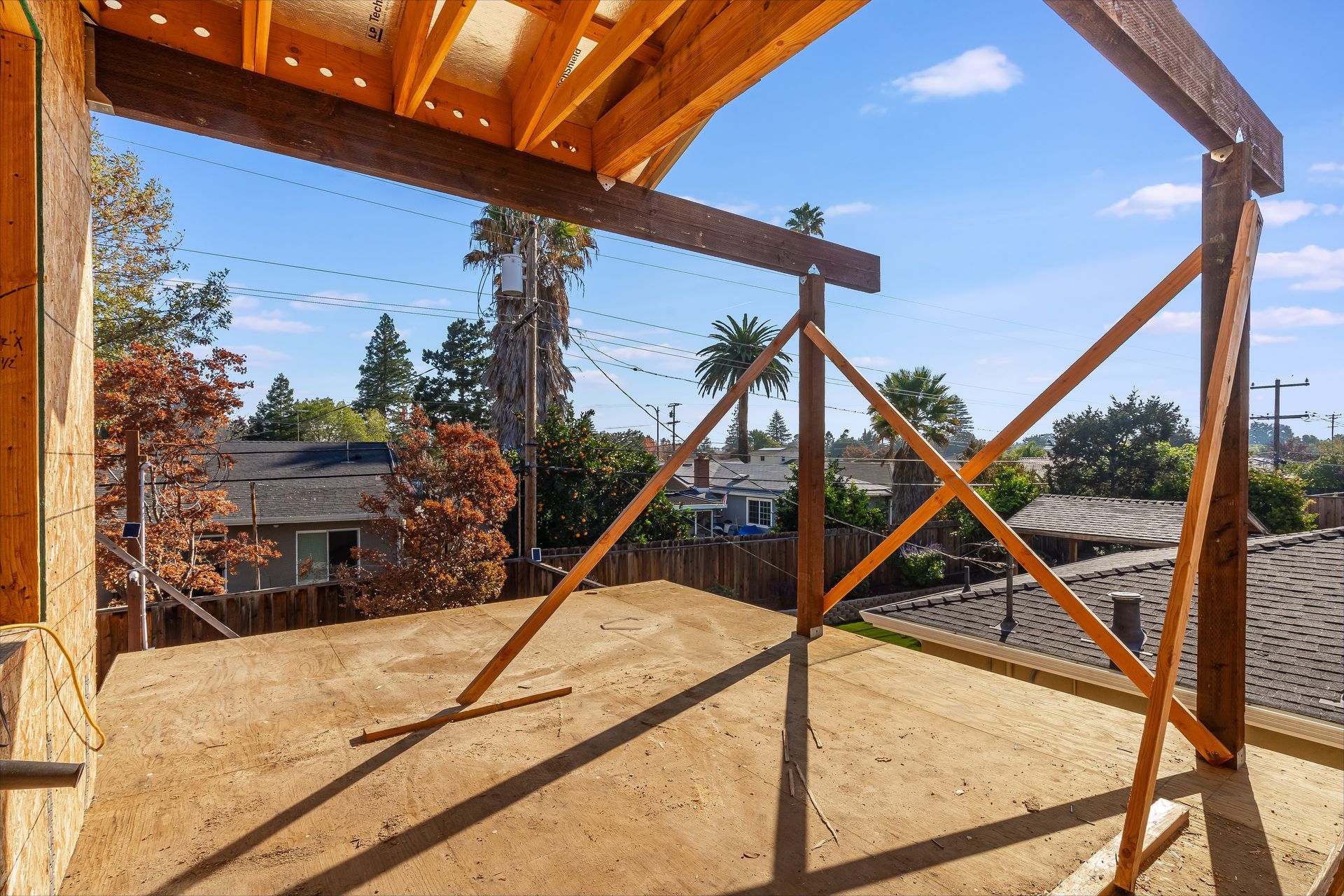 Construction site with wooden framing and supports, overlooking a neighborhood under a blue sky.