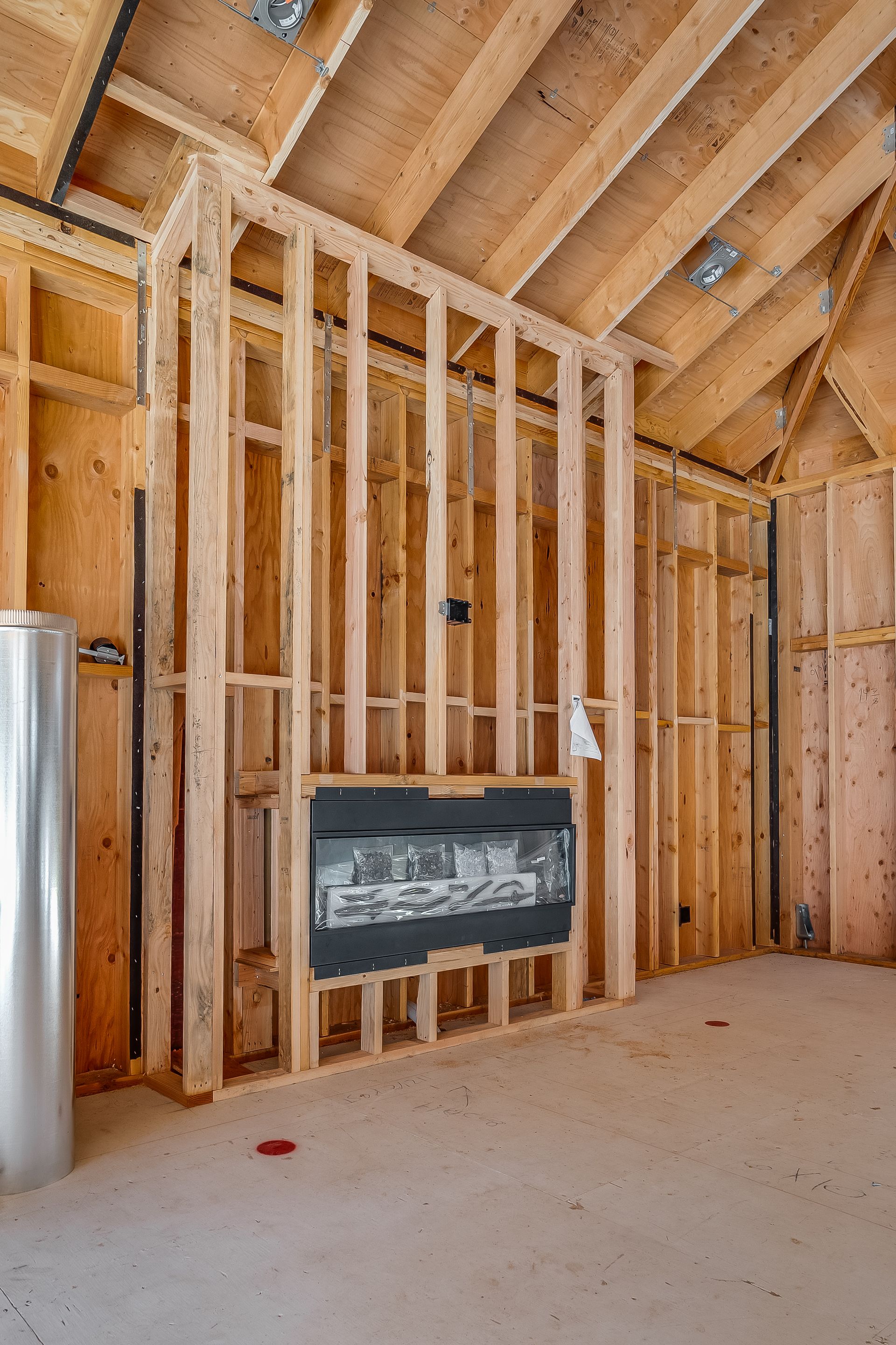 Interior framing of a room with exposed wooden studs, a black electrical panel, and a water heater.