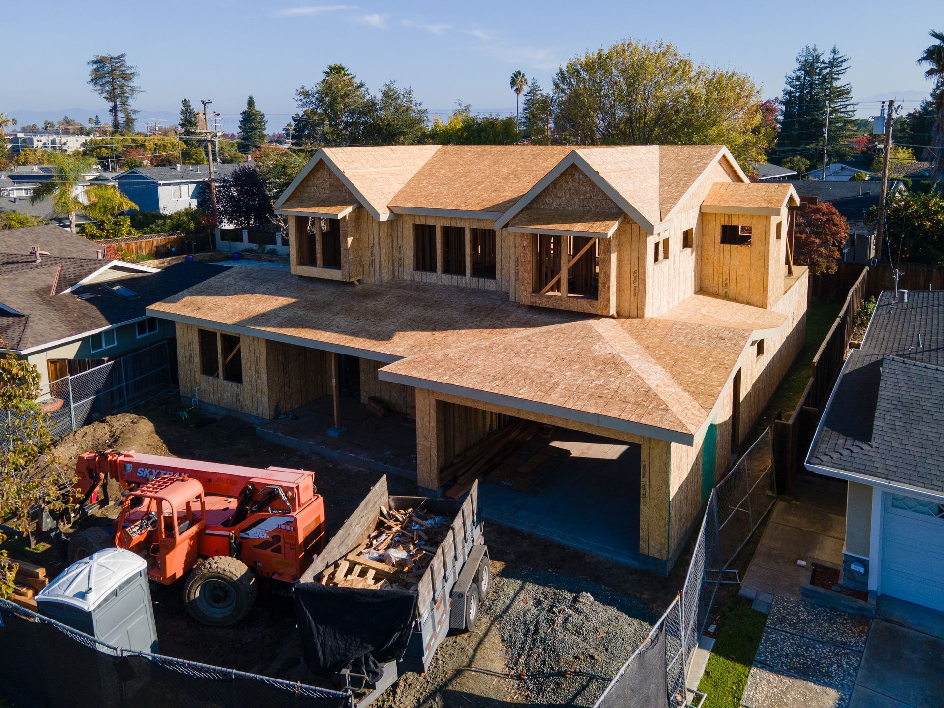 Wooden framed house under construction; orange construction lift and debris nearby.