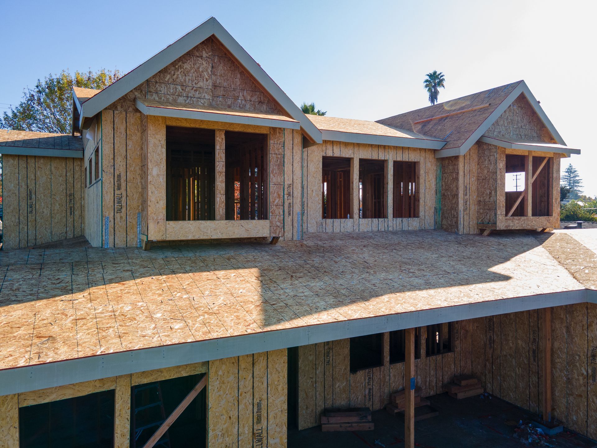House under construction, wood frame with dormers, bare wood, light sky.