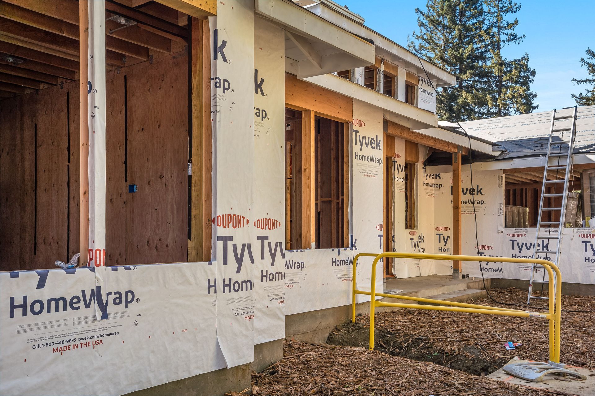 Exterior view of a house under construction with Tyvek wrap and exposed framing.
