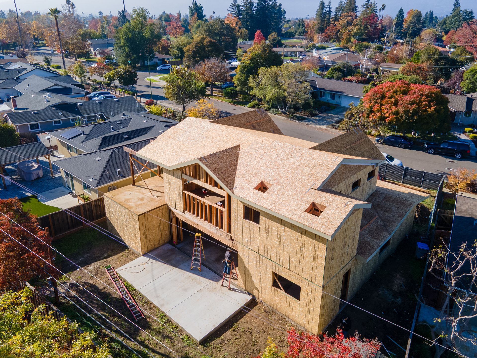 Two-story house under construction, with exposed wooden frame and plywood roof. 
