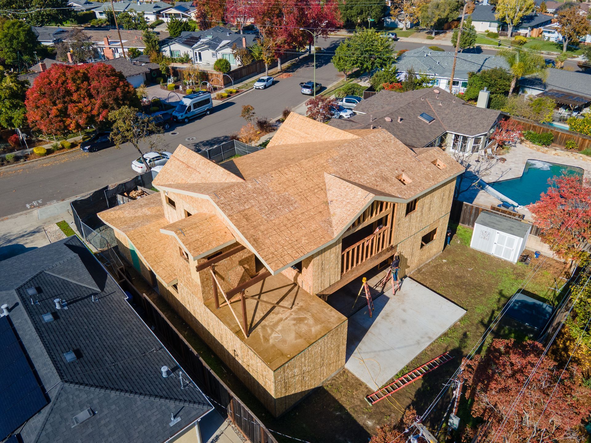 Aerial view of a two-story house under construction with exposed wood framing and a backyard with a pool.