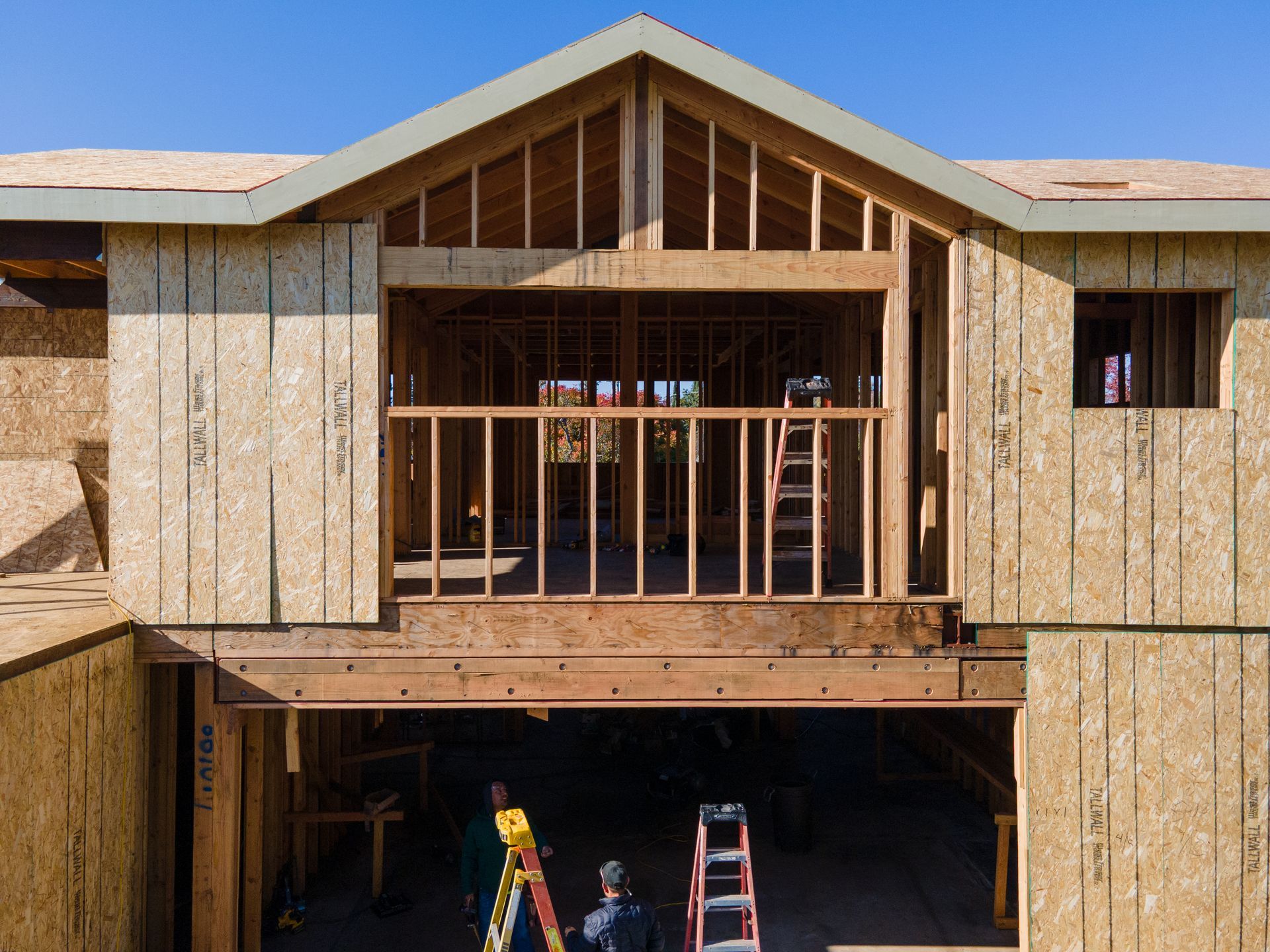 Framing of a house under construction with a balcony, workers, and ladders.
