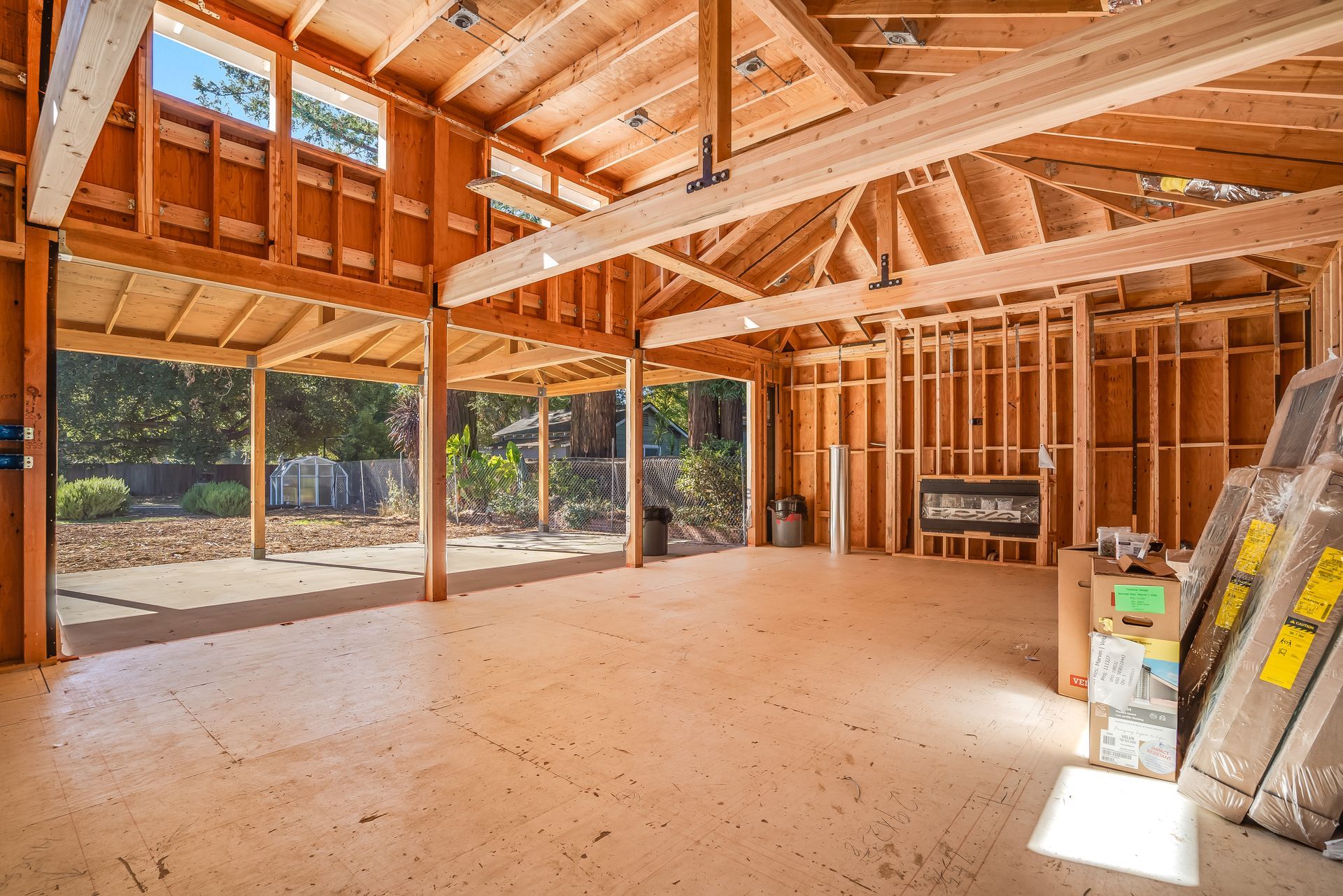 Interior of a wooden framed structure, likely a new build, with concrete flooring and views to an outside yard.