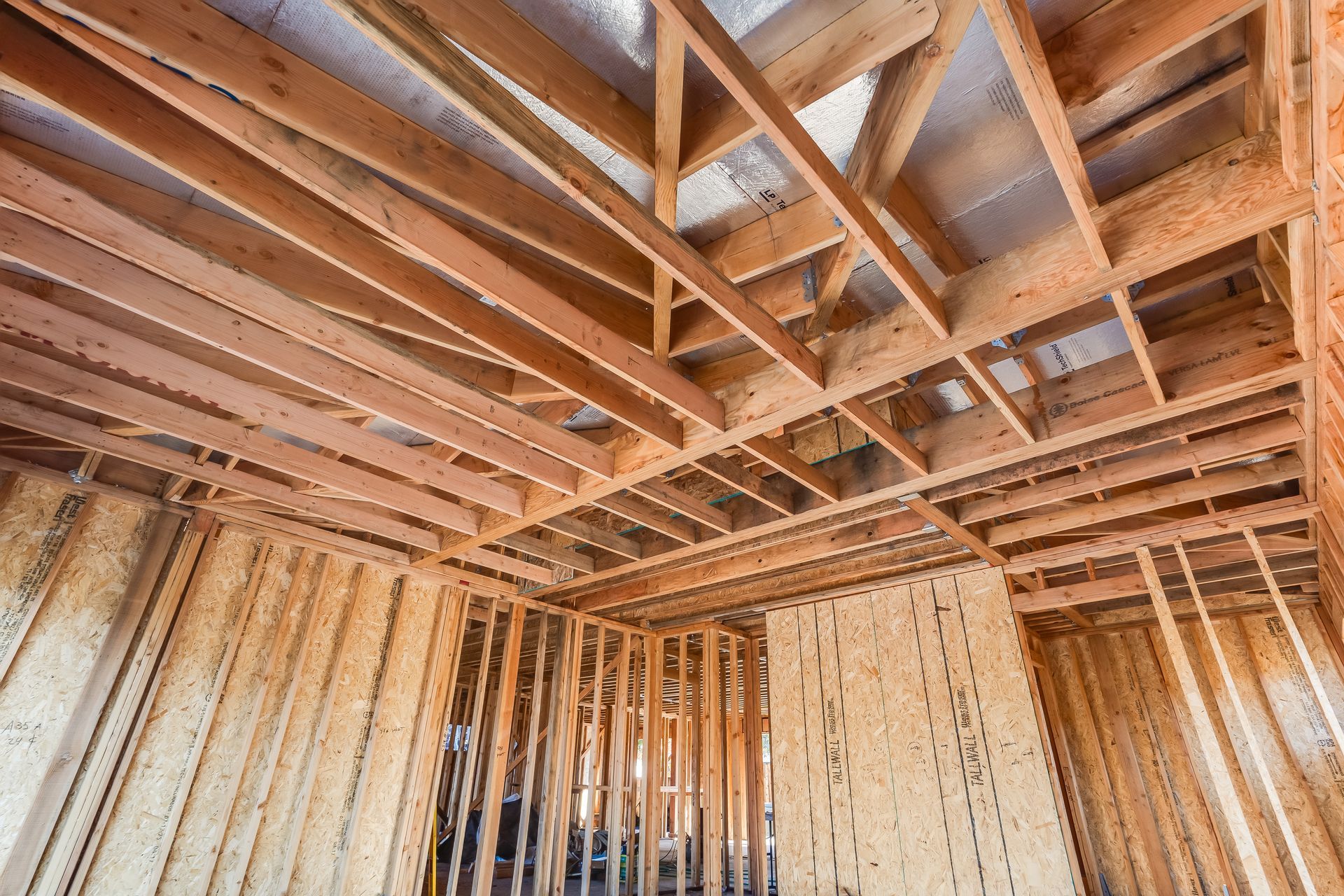 Interior framing of a building under construction, showing wooden studs, rafters, and ceiling beams.