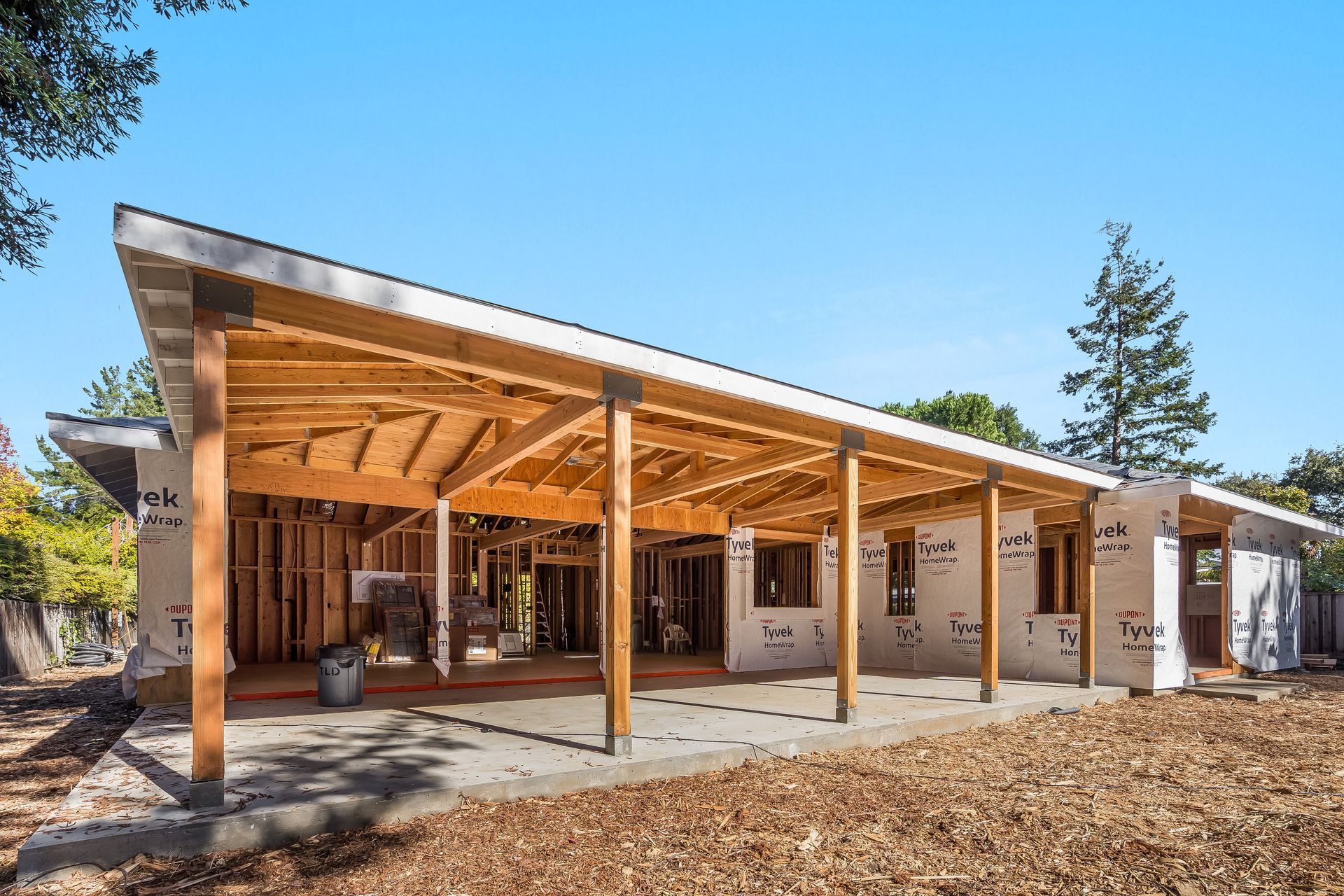 Under-construction home with a wooden porch and framing, surrounded by exposed insulation and clear sky.