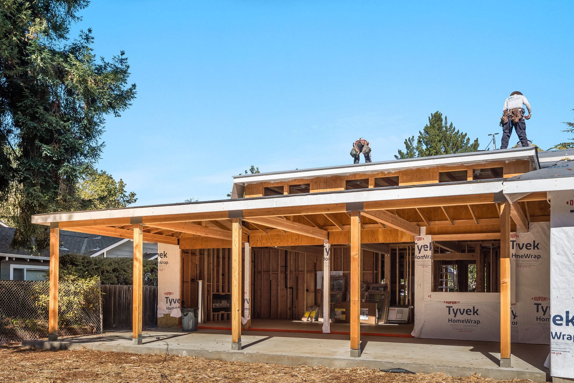 Construction workers on a house, building a wooden porch and roof. Clear blue sky, sunny day.