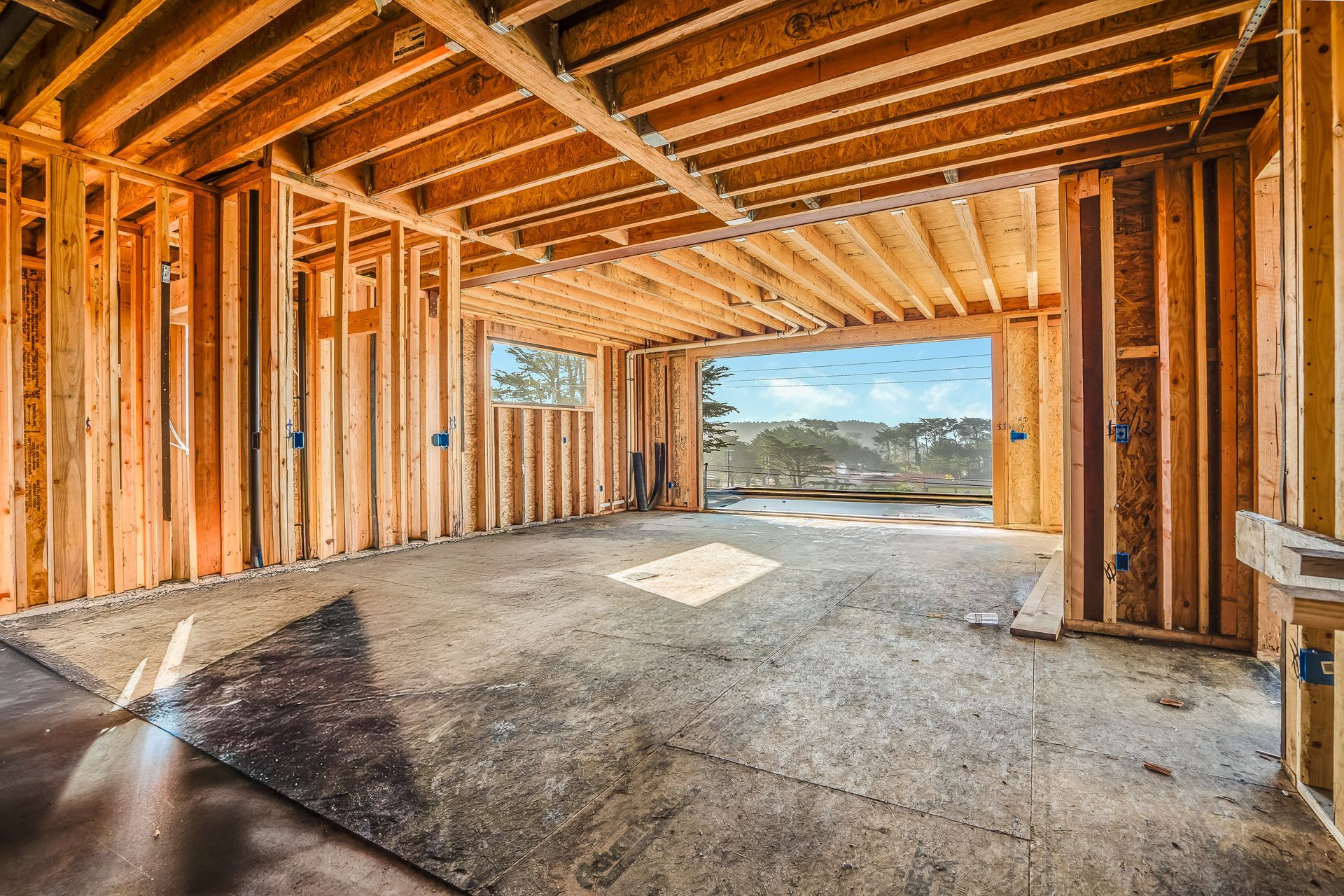 Interior of a house under construction; wooden framing with an open doorway overlooking a bright sky.