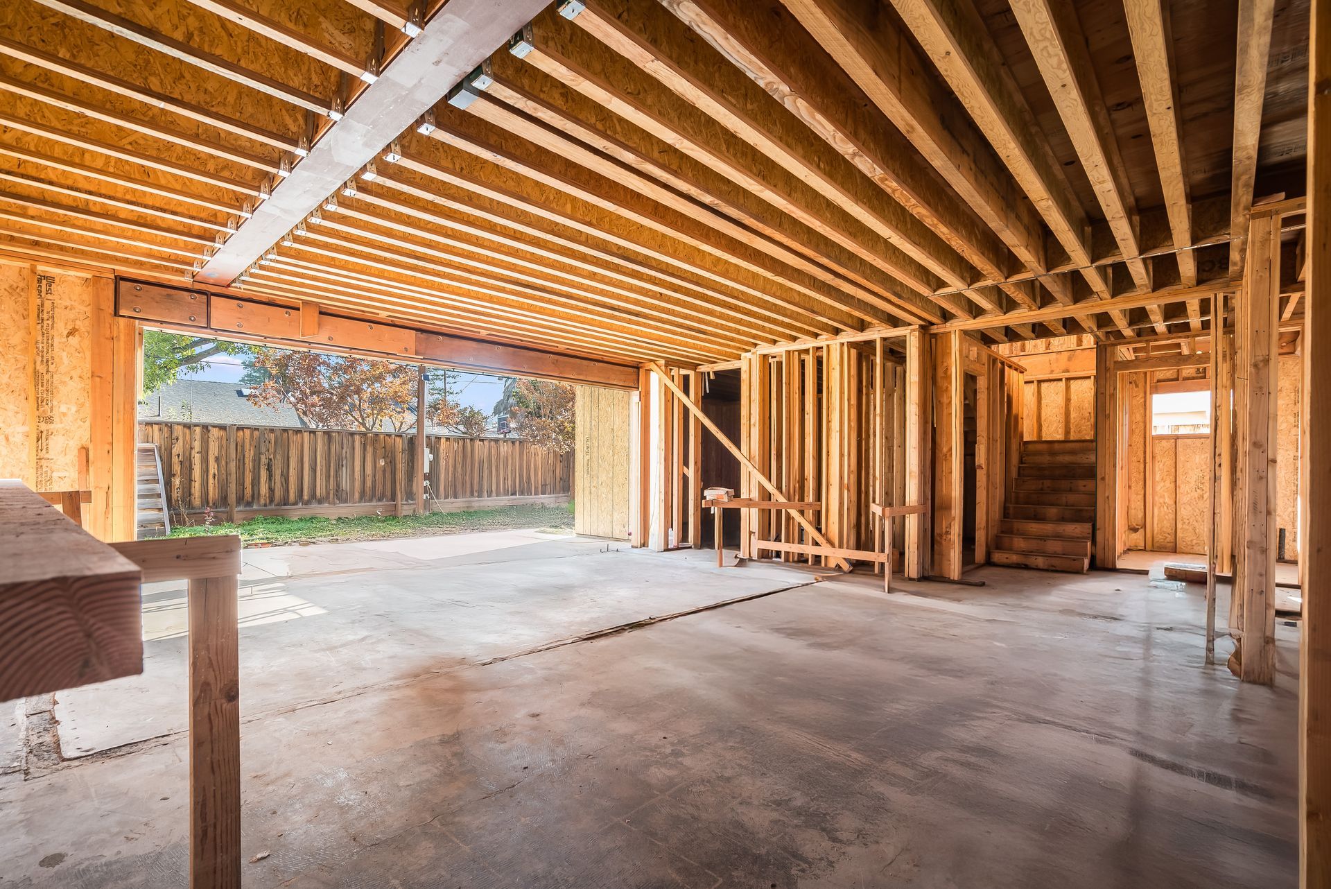 Unfinished wooden structure with concrete floor; open doorway to a fenced yard.