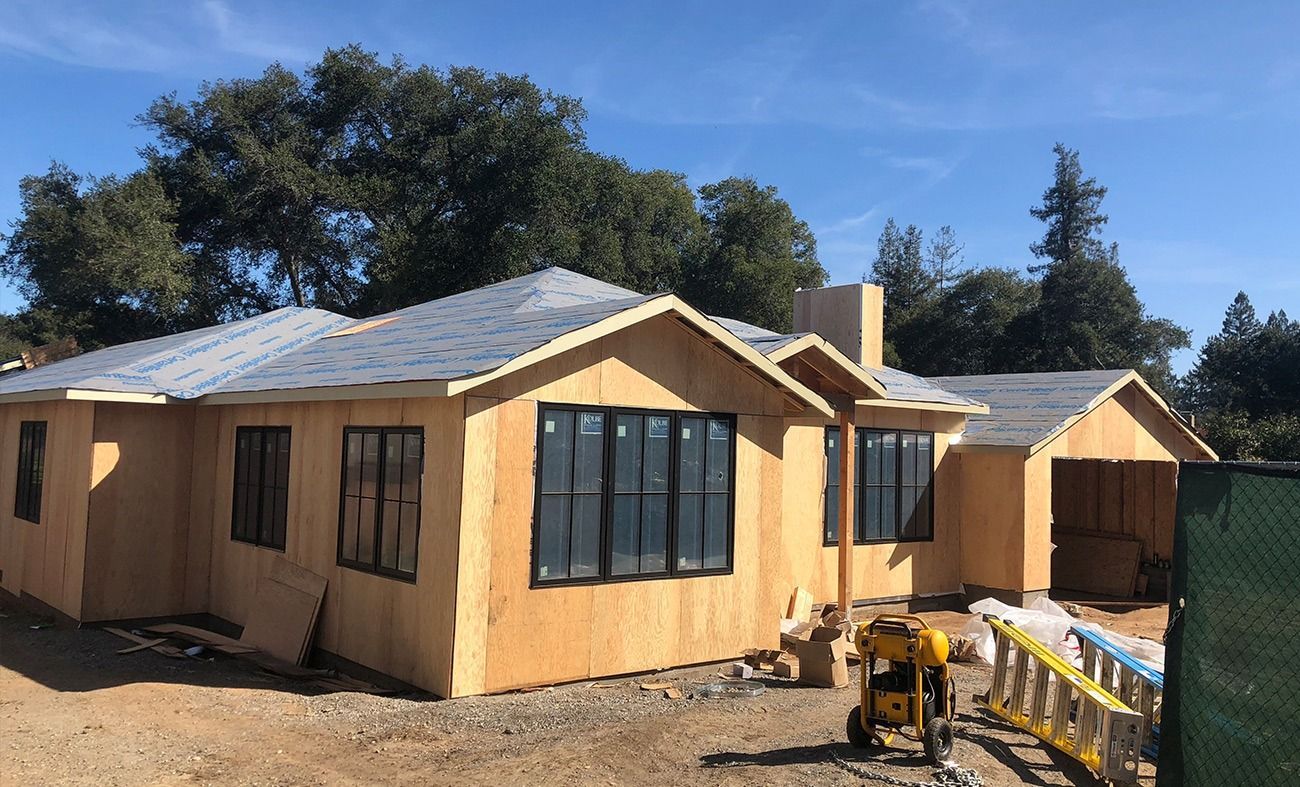 House under construction with exposed wood framing, black windows, and gray roof.